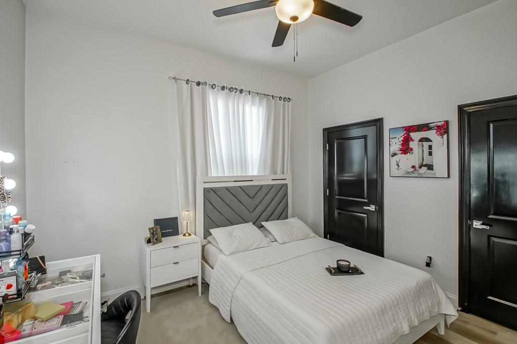 Bedroom with a white bed, chevron-patterned headboard, sheer curtains, and black paneled doors.