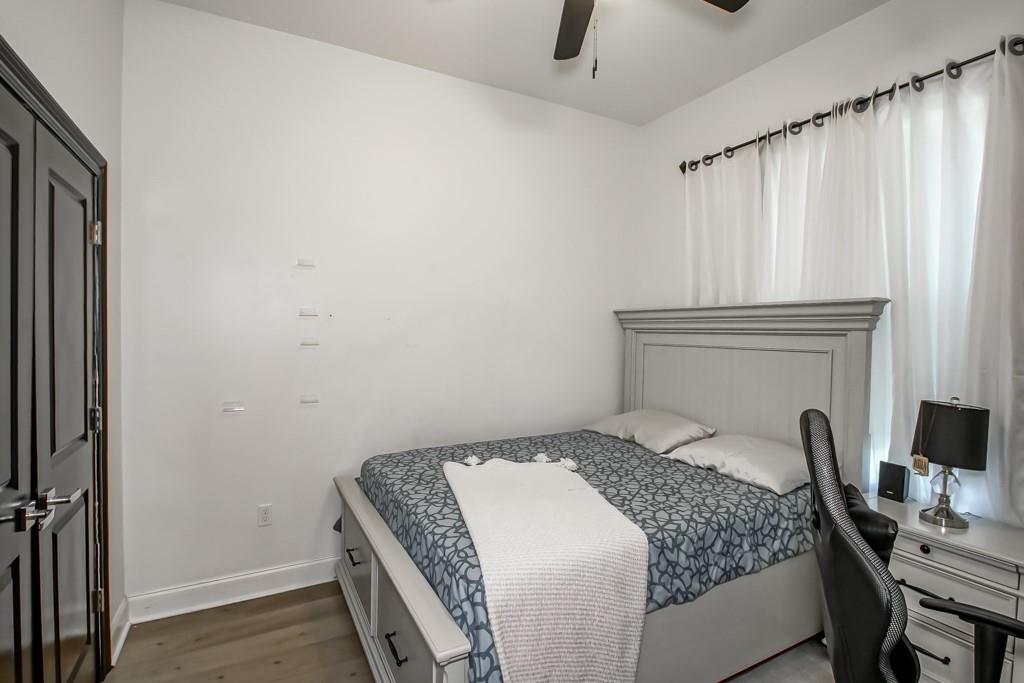Bedroom with a gray patterned bed, tall paneled headboard, and white curtains.