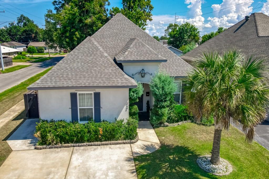 Home with a multi-gabled roof, concrete driveway, landscaped front yard, and palm tree.