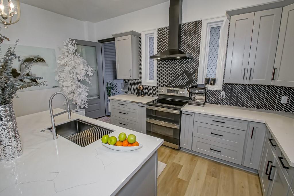 Updated kitchen with gray cabinets, black herringbone backsplash, stainless appliances, and a large island sink.