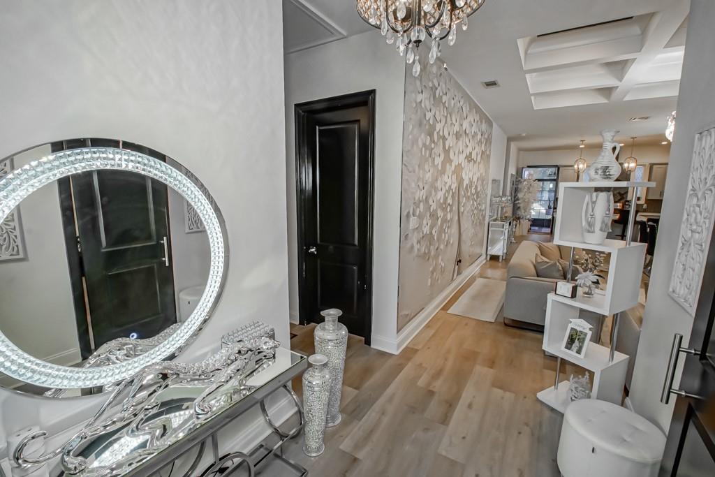 Entry hall with a mirrored console, crystal chandelier, and light wood floors leading to a living area.
