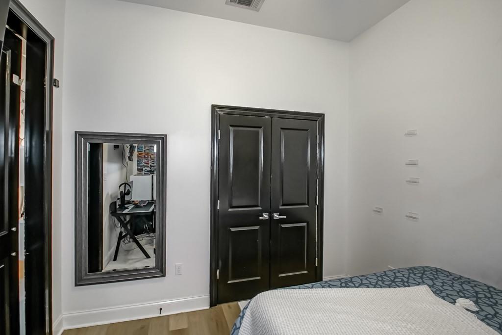Bedroom with dark double doors, a mirror reflecting a desk, and blue patterned bedding.
