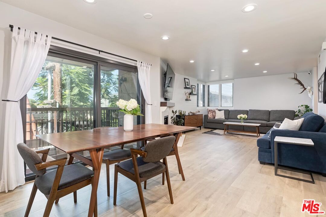 Open-plan living and dining room with a wooden table beside sliding glass doors overlooking trees.