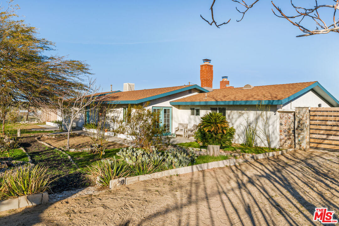 Single-story stucco home with teal roof trim, brick chimneys, desert landscaping, and a small patio.