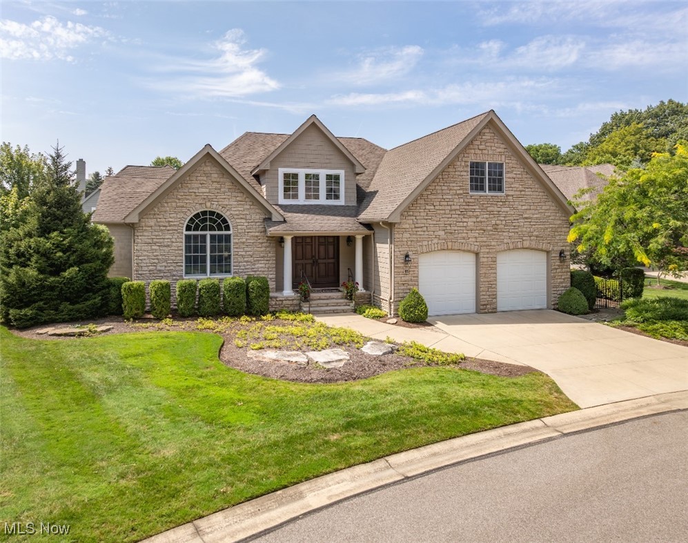 Stone-front two-story home with an arched window, landscaped lawn, and two-car garage.