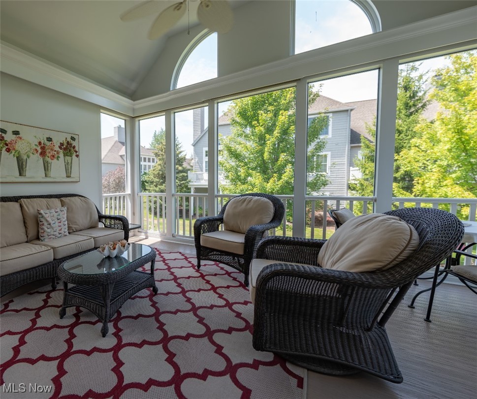 Sunroom with wicker seating, a patterned rug, and tall windows overlooking trees.