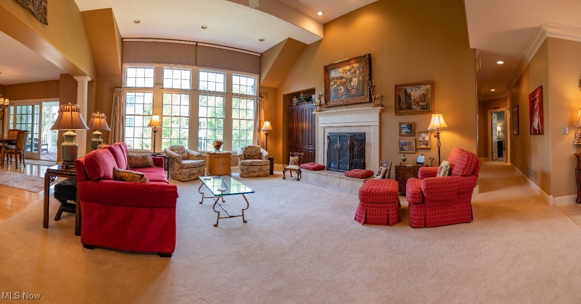 Furnished living room with vaulted ceiling, large windows, white fireplace, and red seating.