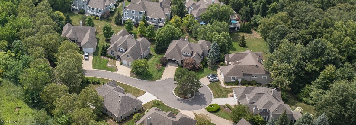 Aerial view of detached homes around a tree-centered cul-de-sac, surrounded by mature trees.