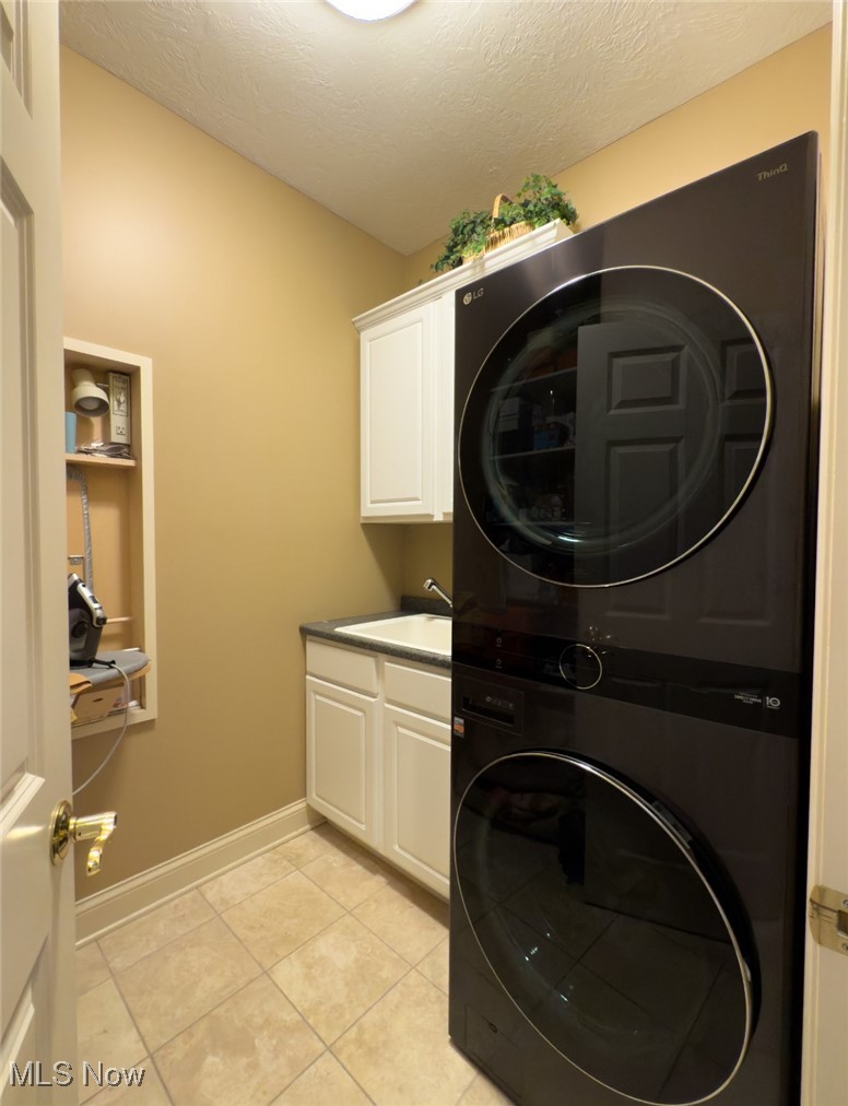 Laundry room with a black stacked washer and dryer beside white cabinets and a utility sink.