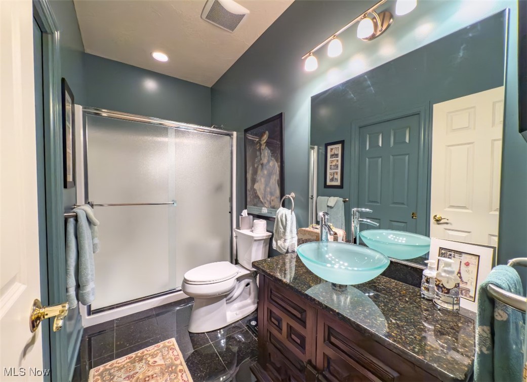 Bathroom with teal walls, glass shower, and double turquoise vessel sinks on a dark vanity.