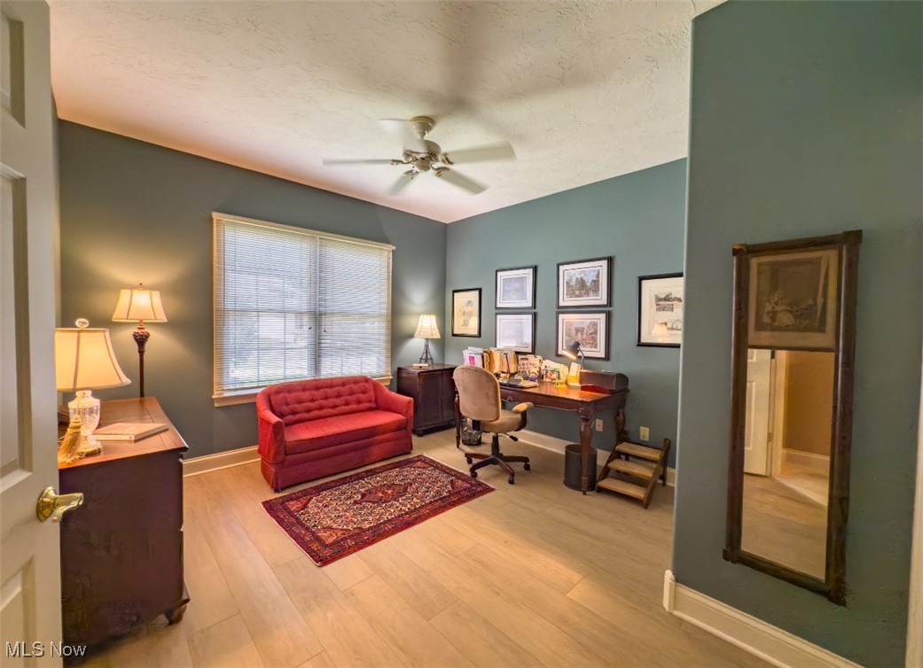 Furnished home office with a red loveseat, wooden desk, and large window with blinds.