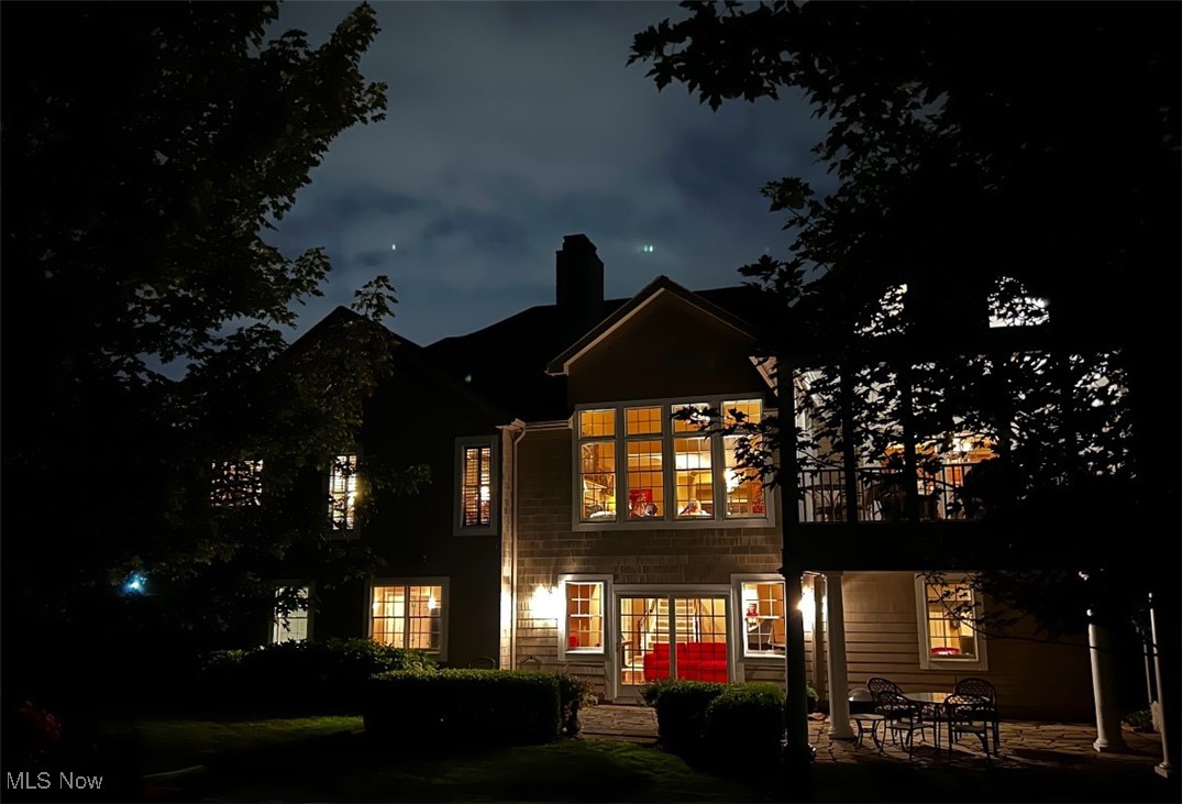 Two-story house glowing warmly at night, with a stone patio and outdoor seating.