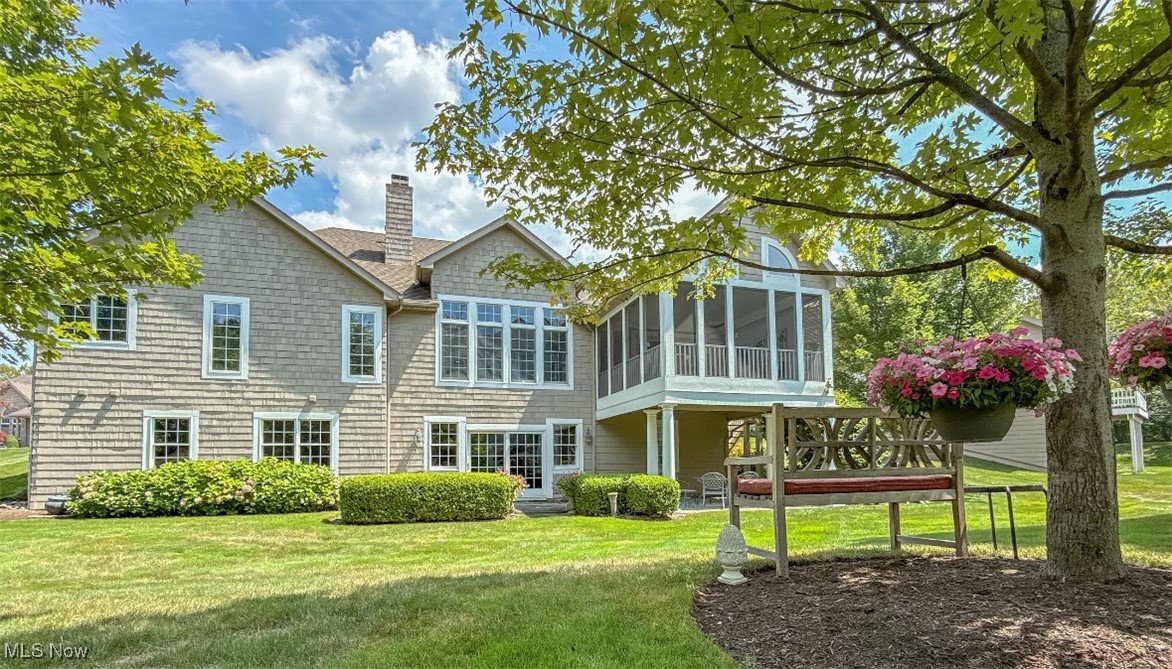 Rear of a shingle-sided house with a raised screened porch, lawn, and shaded garden bench.