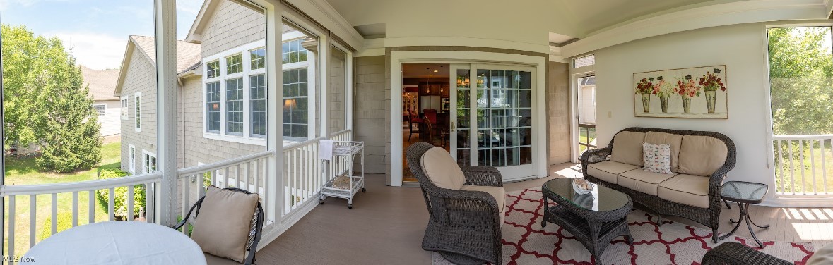 Covered porch with wicker seating and a red-and-white rug overlooking a green yard.