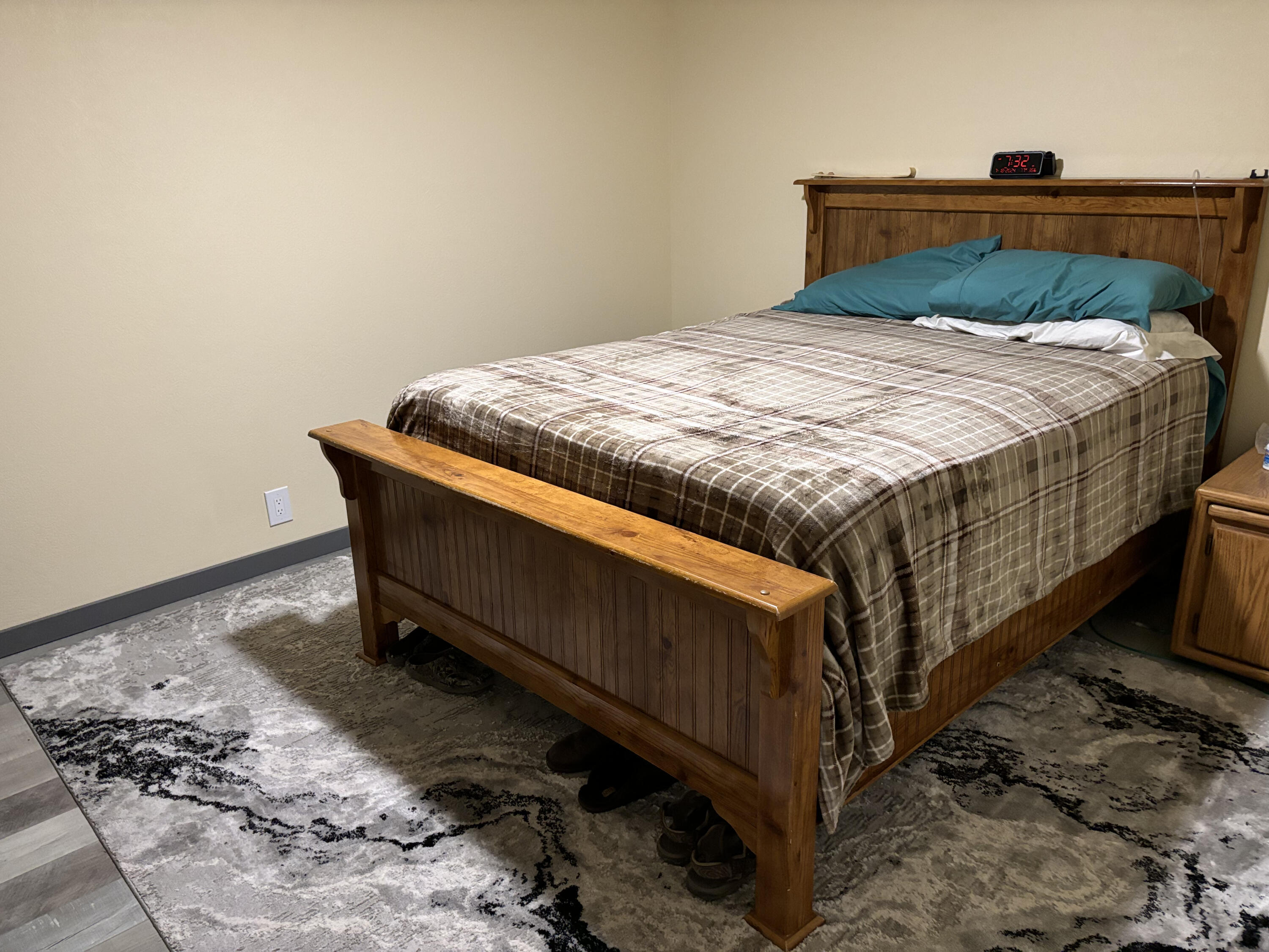 Bedroom with a wooden bed, plaid bedding, teal pillows, and a patterned gray rug.