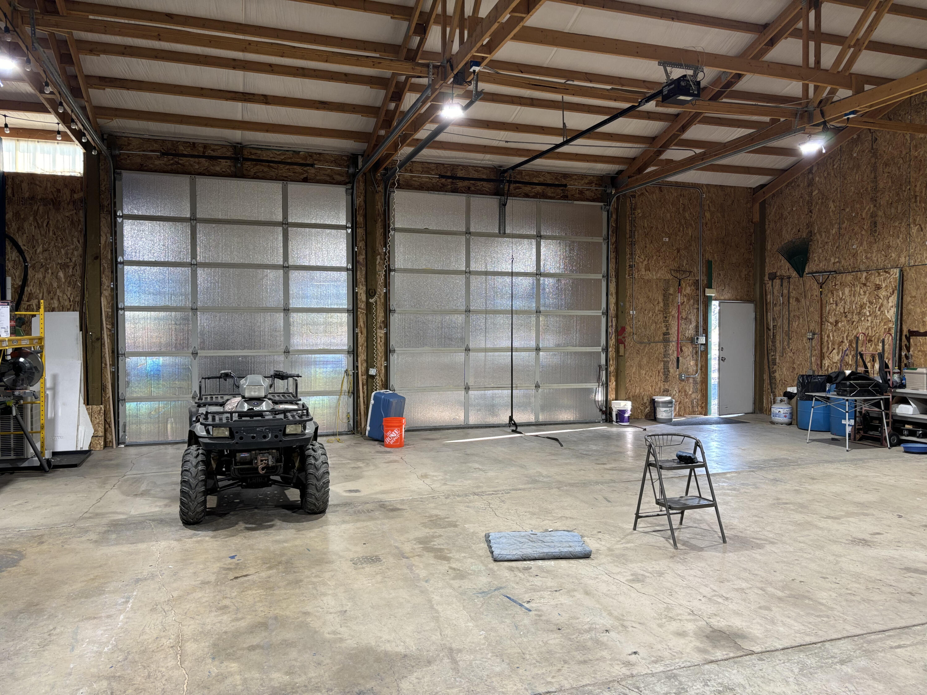 Large garage with two overhead doors, exposed timber trusses, and an ATV on the concrete floor.