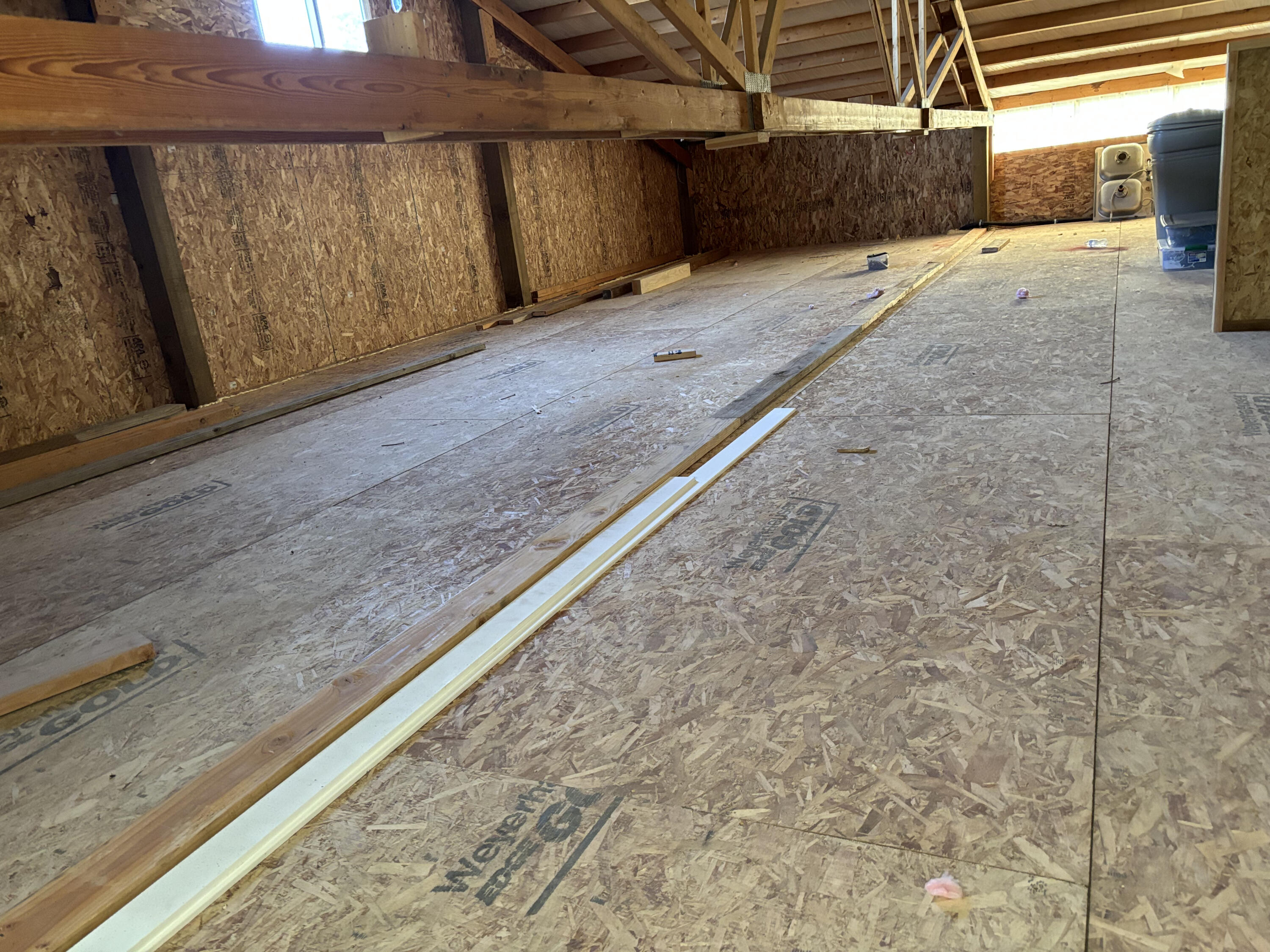 Unfinished interior with exposed roof trusses, OSB walls and flooring, and construction materials on the floor.
