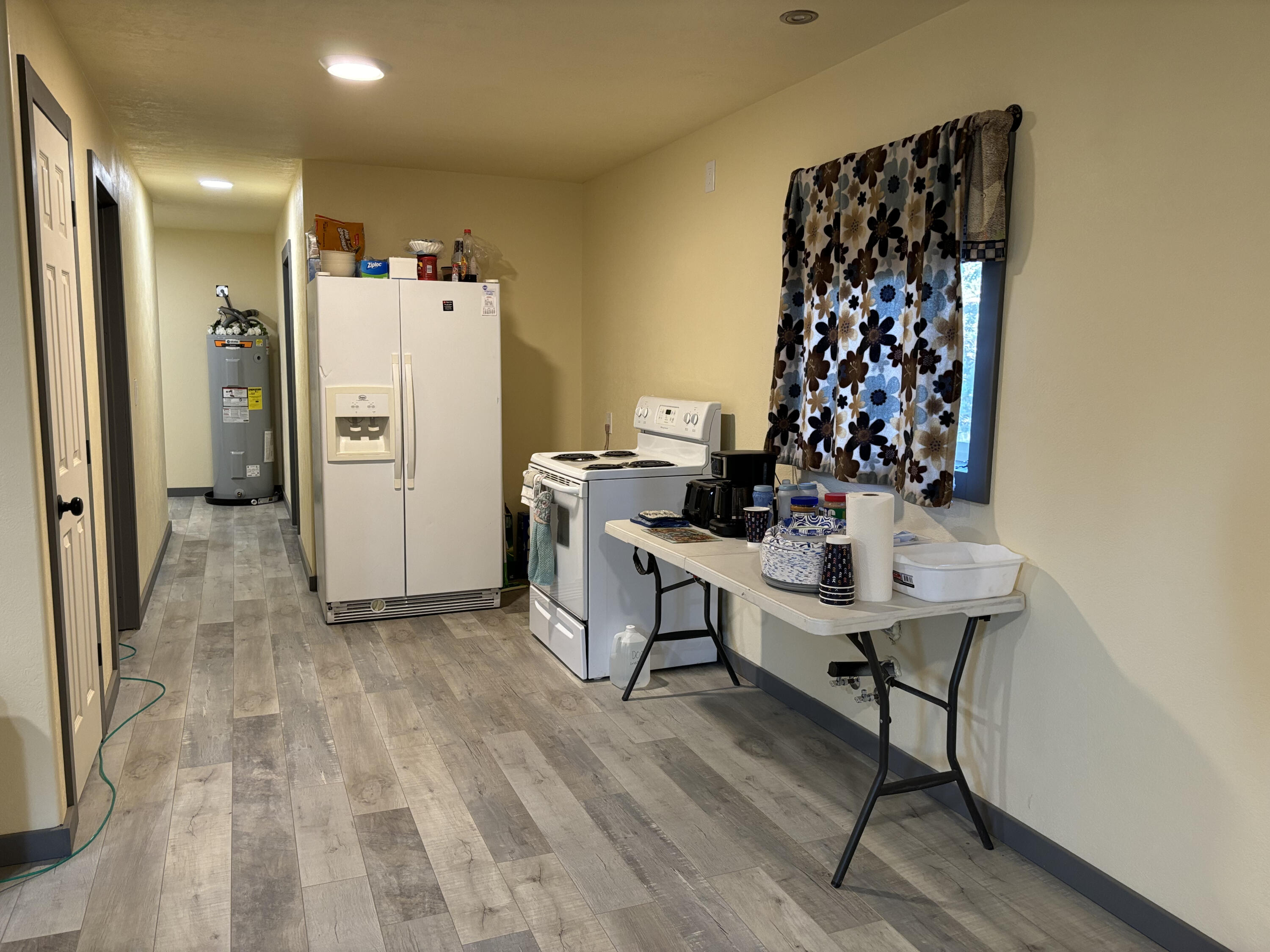 Utility room with a refrigerator, electric range, water heater, and folding table.