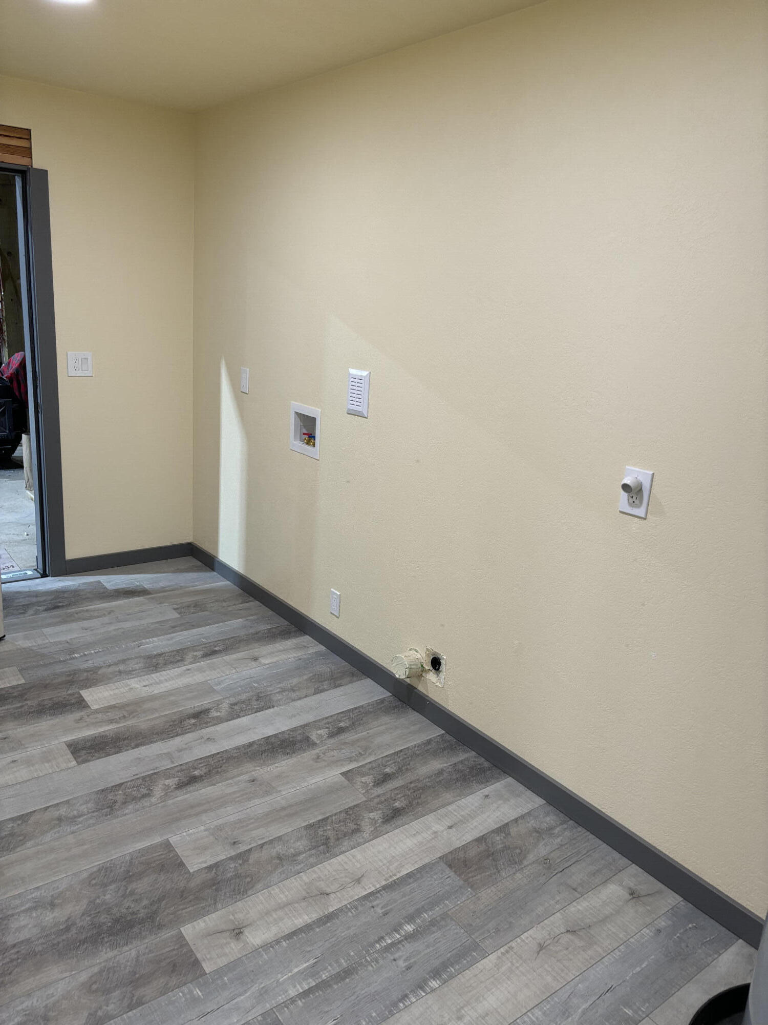 Empty laundry area with gray plank flooring and wall-mounted washer and dryer connections.