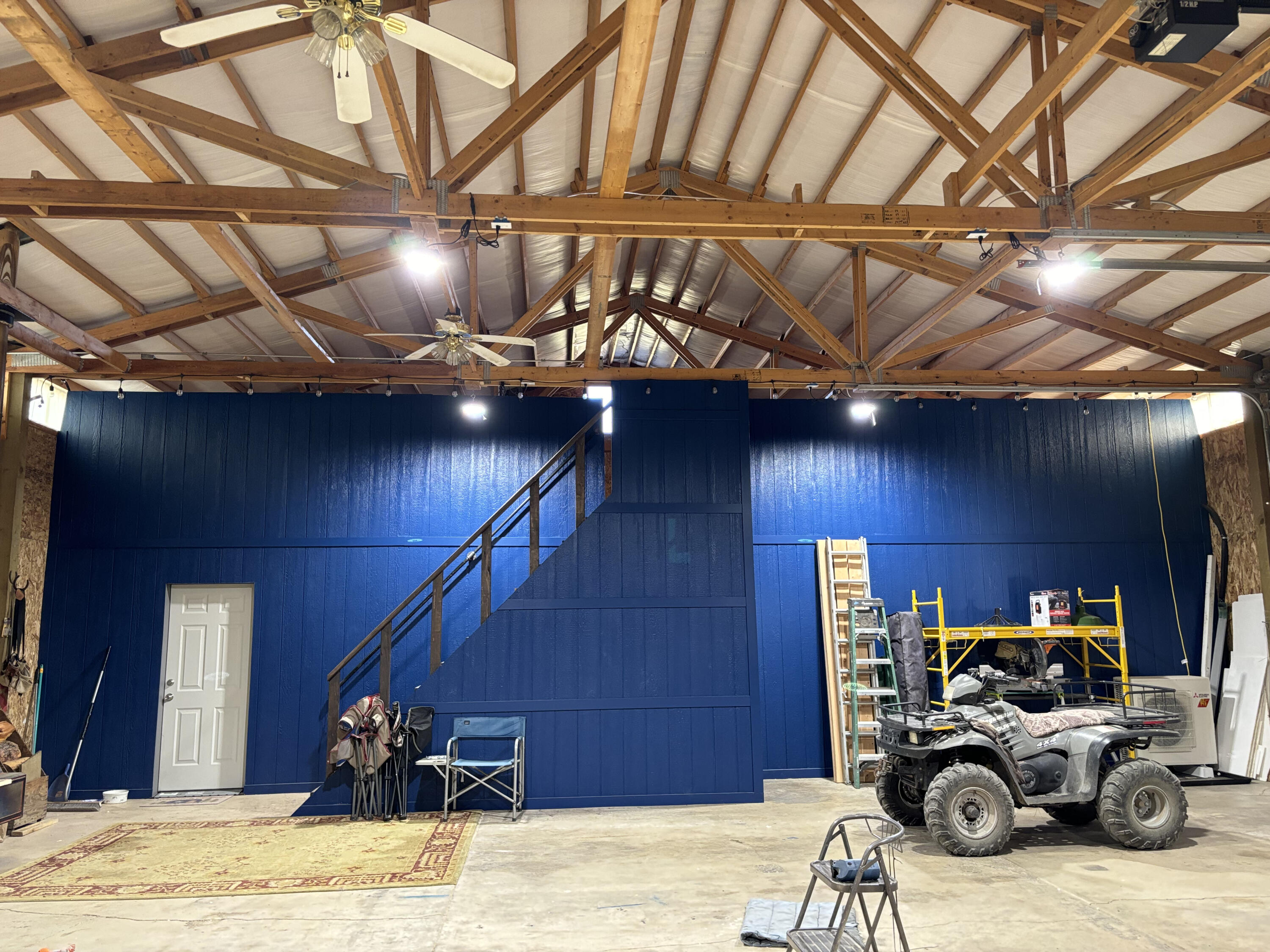 Large shop with exposed timber trusses, a staircase to an upper level, and an ATV.