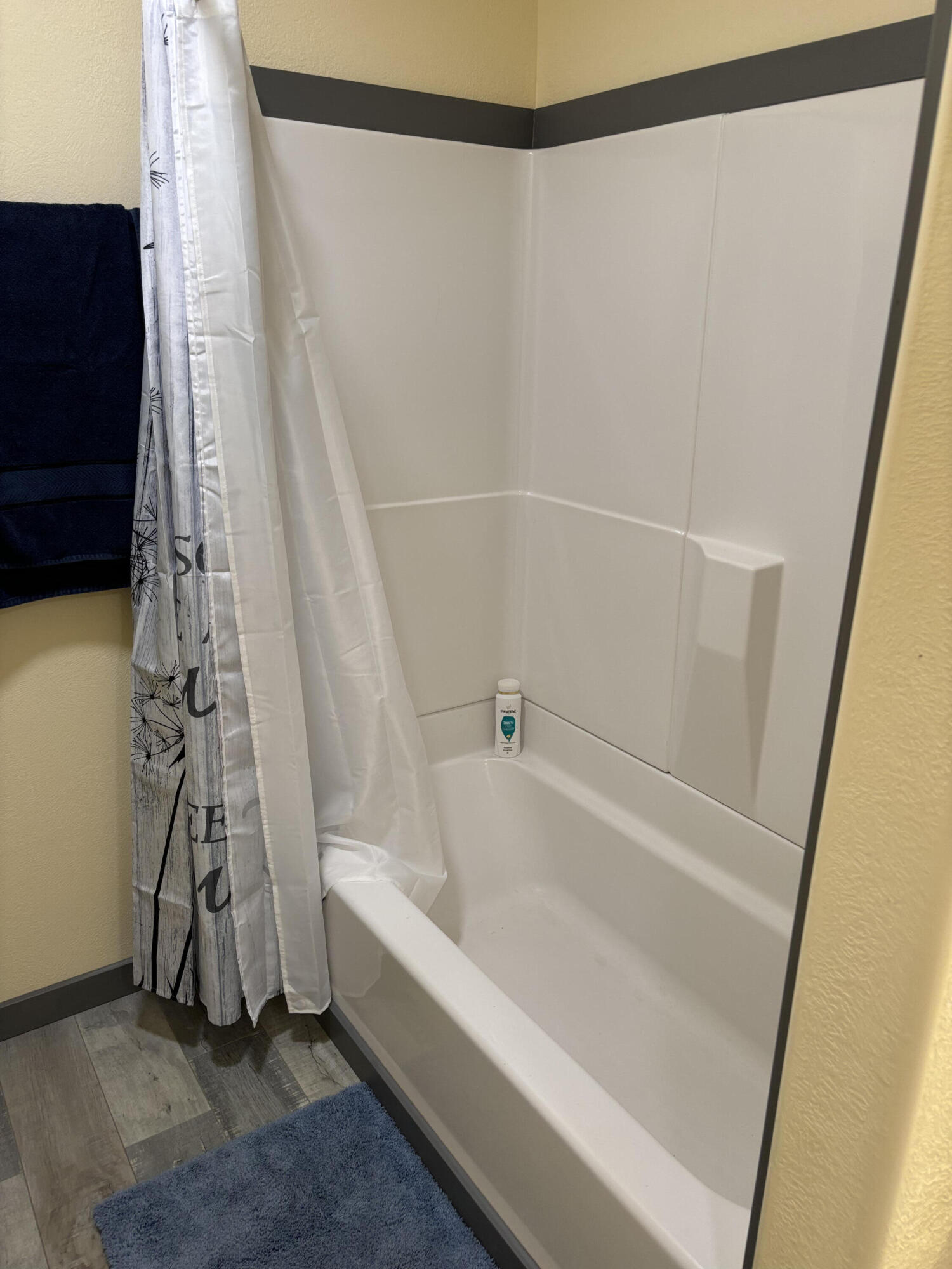 Bathroom tub and molded surround with a patterned shower curtain and blue bath mat.