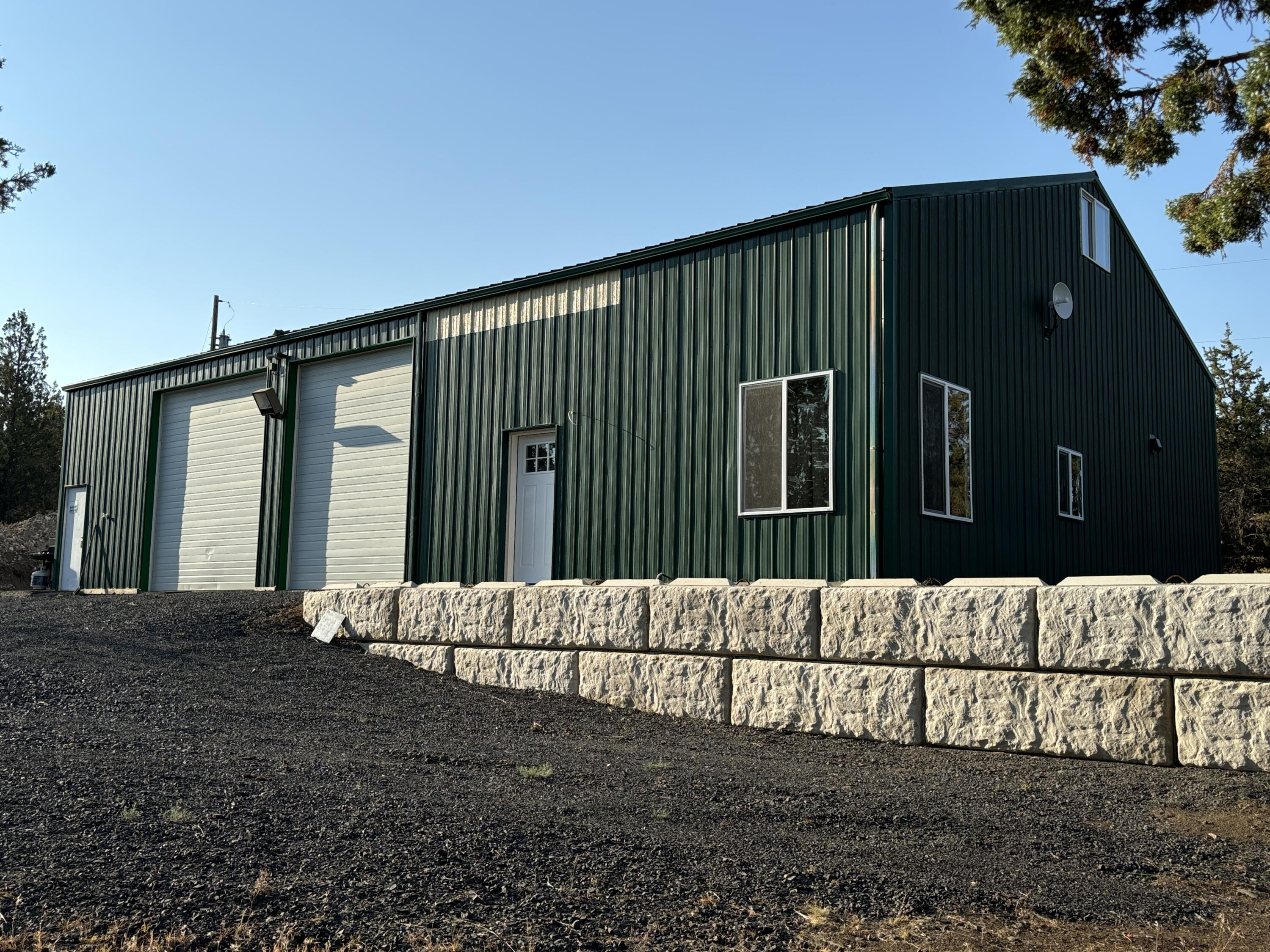 Dark green metal building with two garage doors and a stone retaining wall in front.
