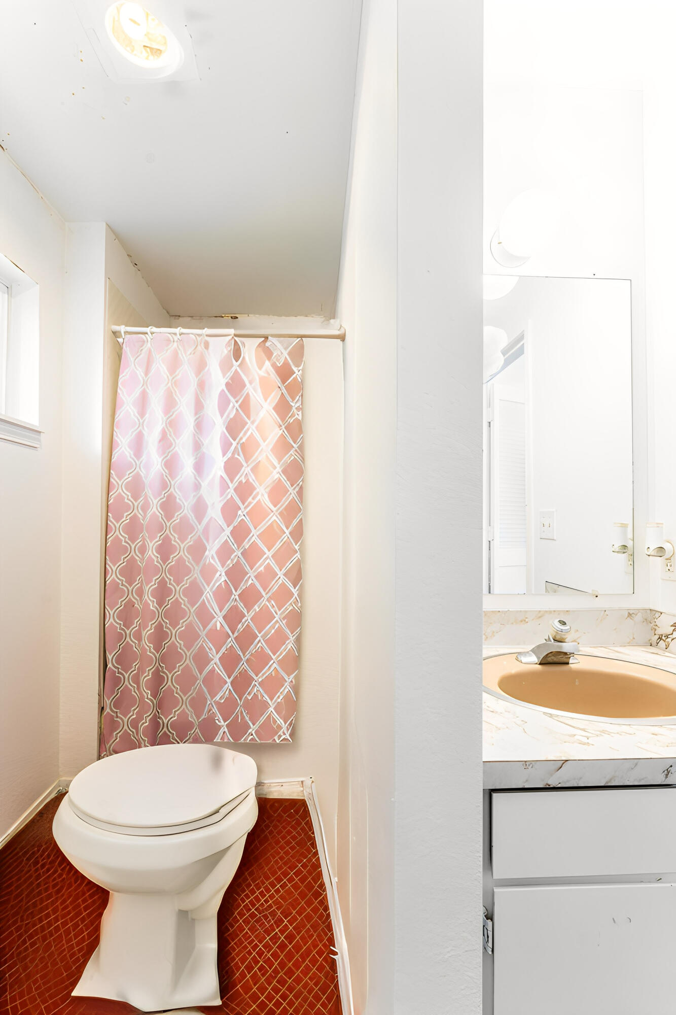 Bathroom with a pink patterned shower curtain, white toilet, and vanity sink.