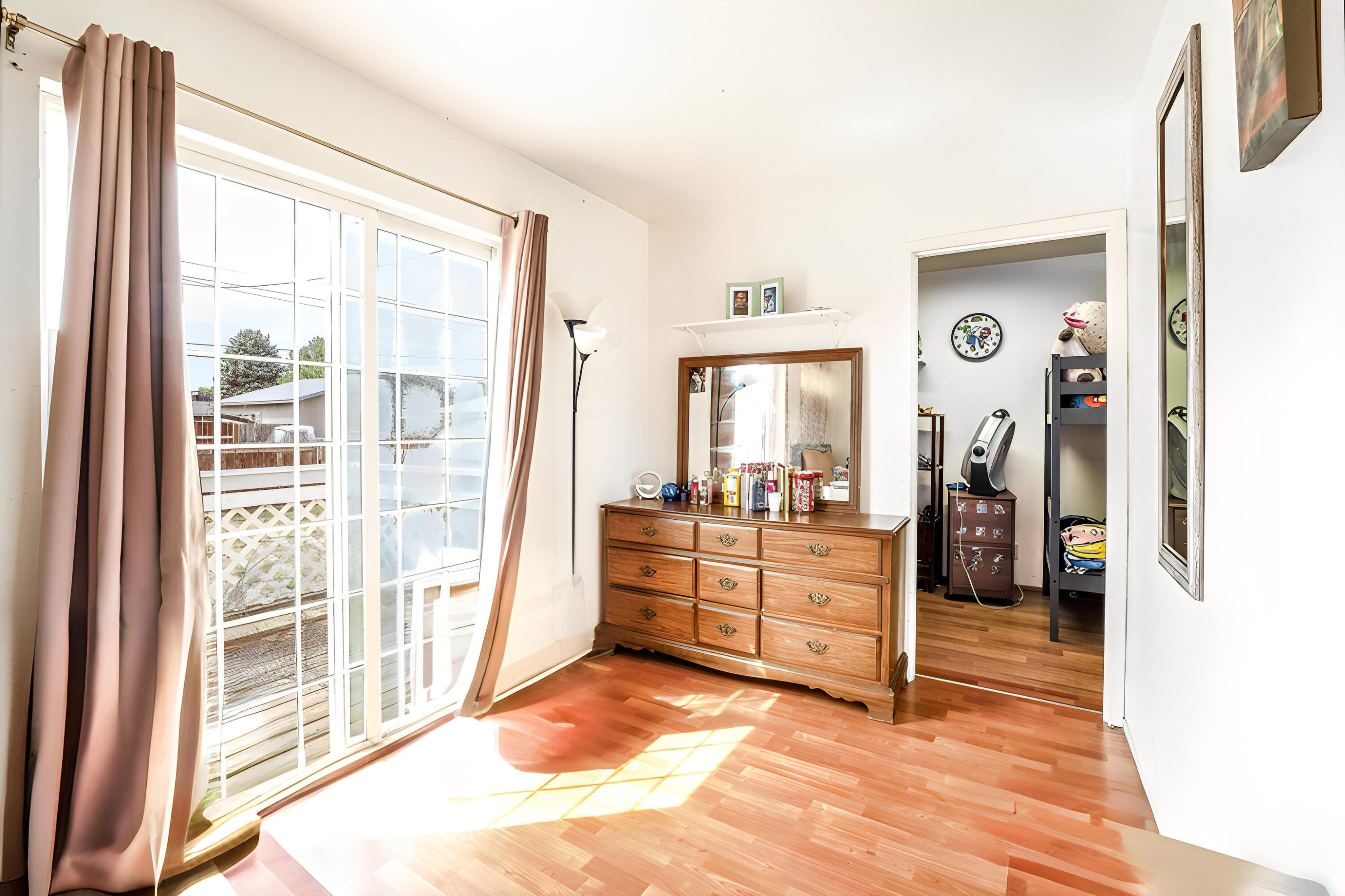 Bedroom with a wooden dresser and large sliding glass door opening toward a deck.