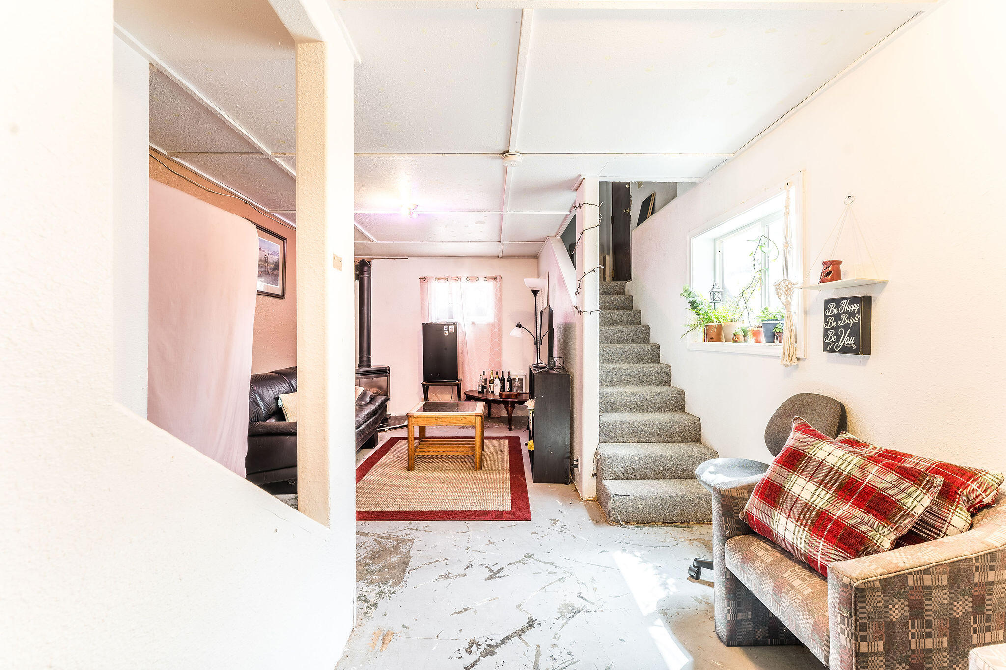 Basement sitting area with carpeted stairs, a bright window, and plaid-cushioned seating.