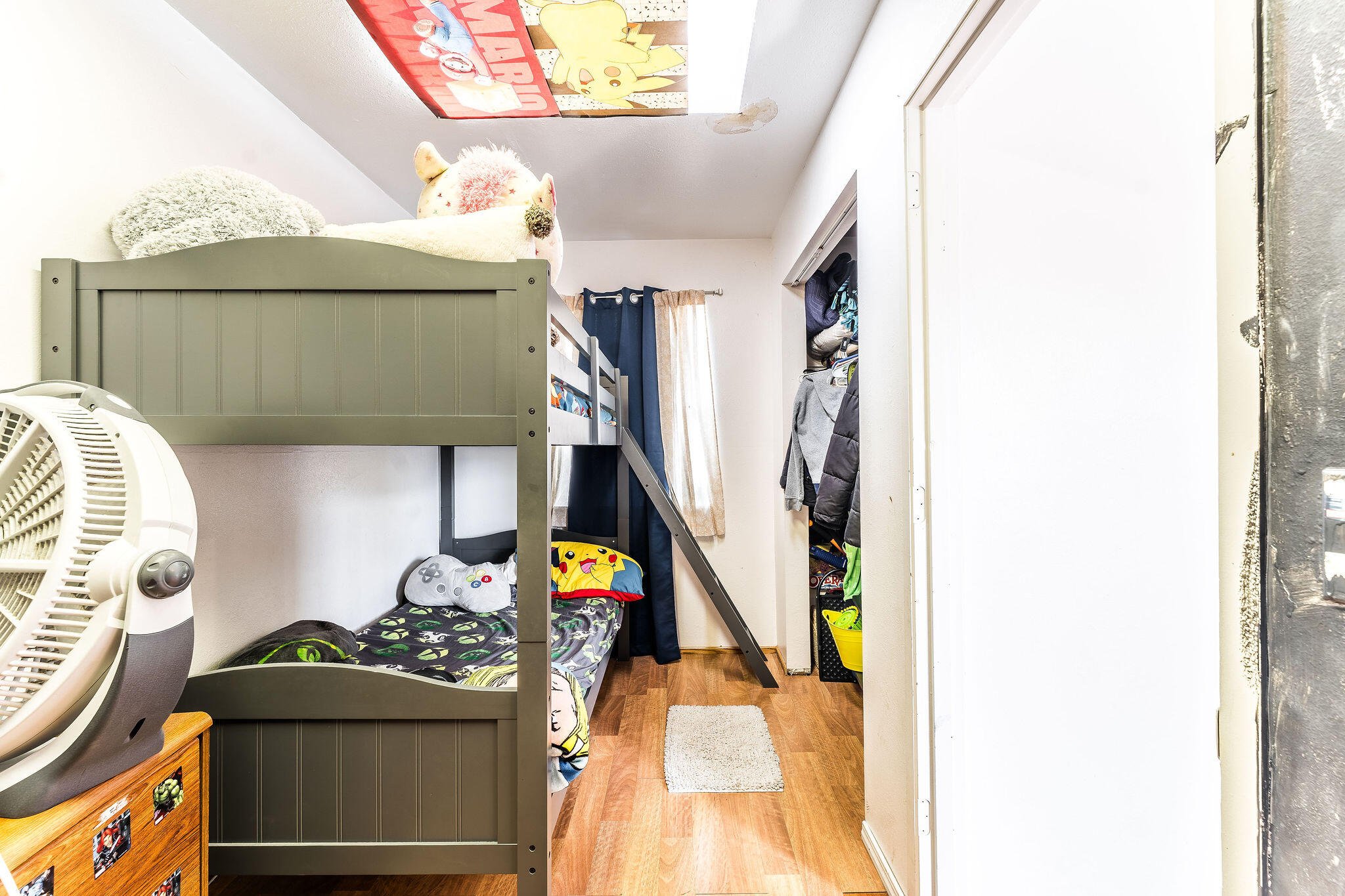 Child’s bedroom with a dark green bunk bed, colorful bedding, and an open closet.