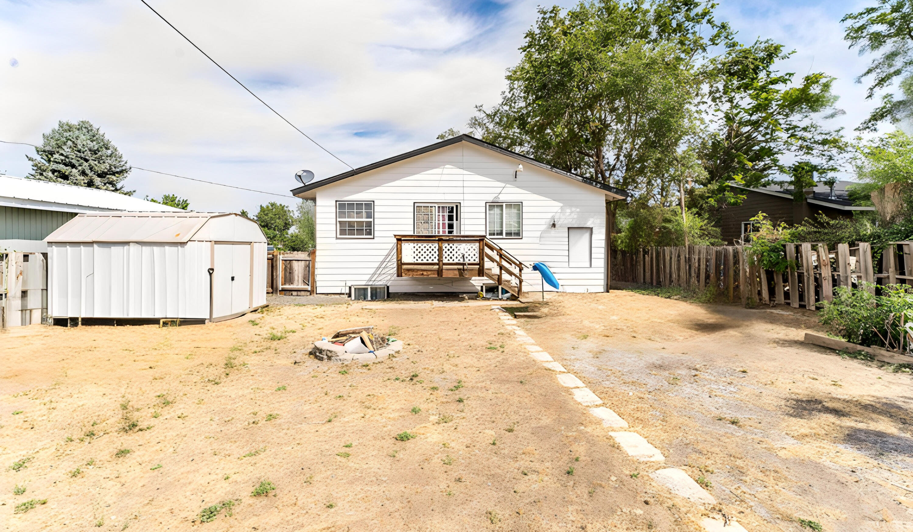 White house rear with a raised deck, large storage shed, and dry fenced yard.