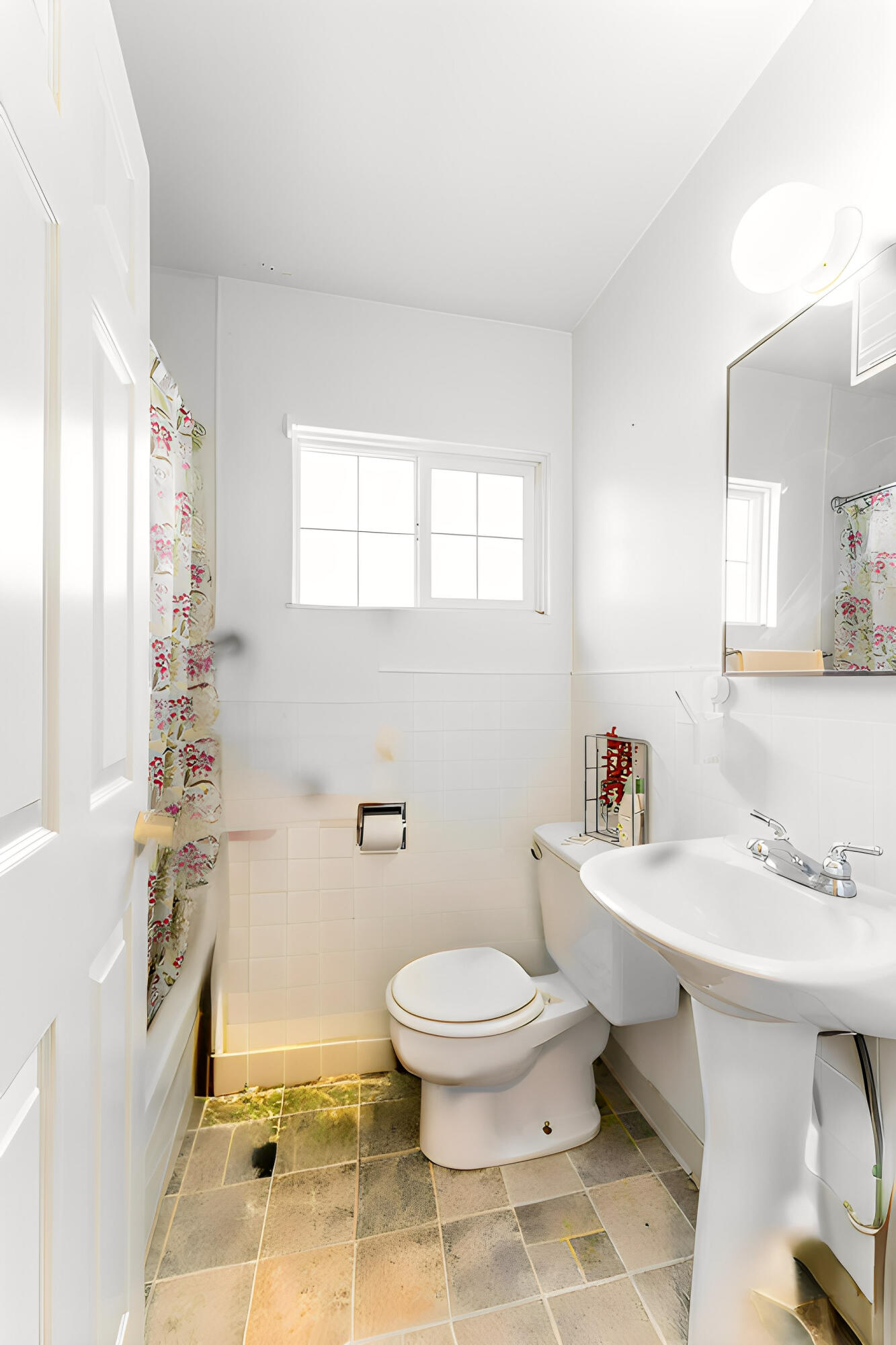 Bathroom with a toilet, pedestal sink, floral shower curtain, and window.