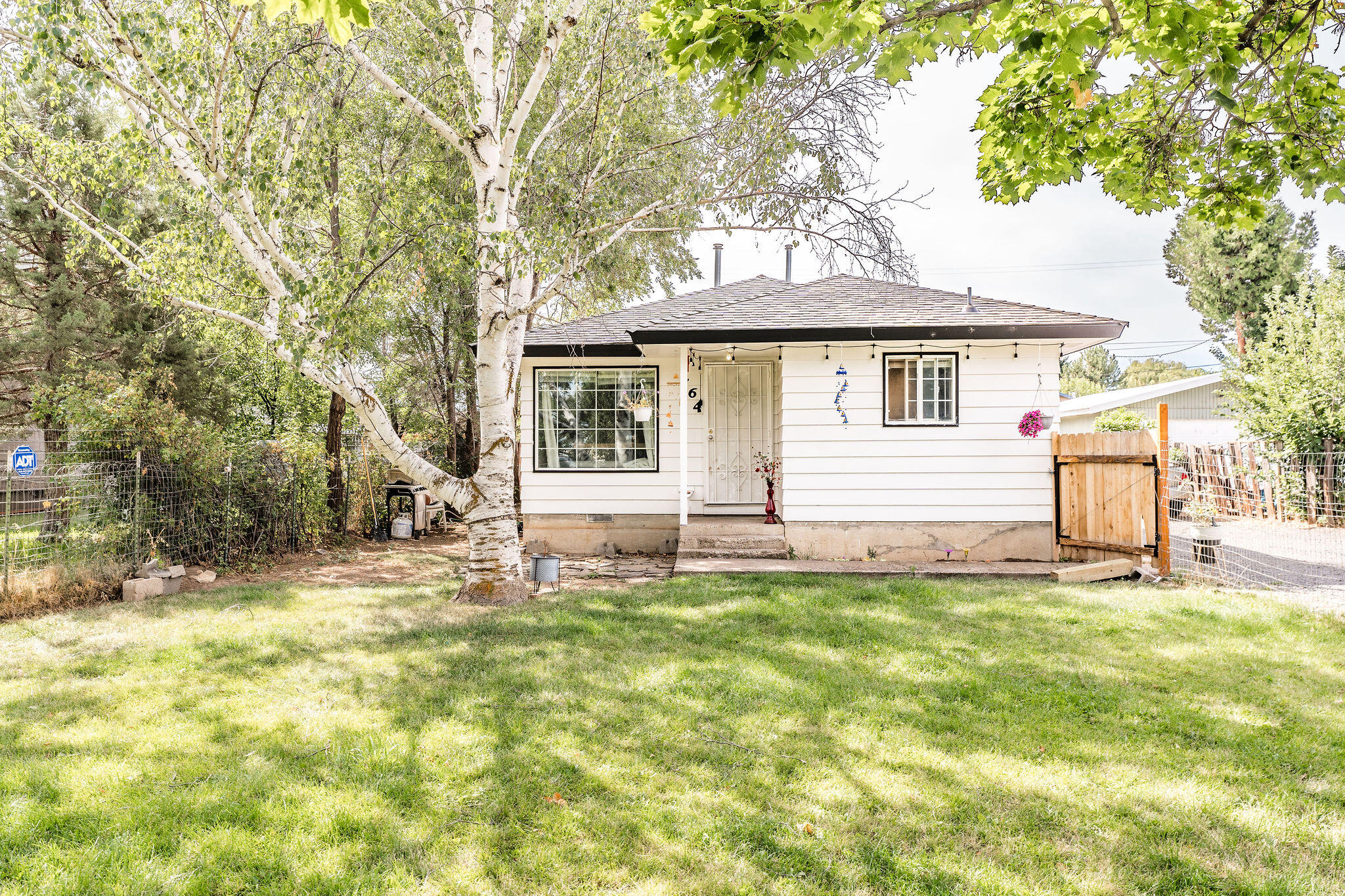 Small white house with front steps and a tree-shaded grassy lawn.