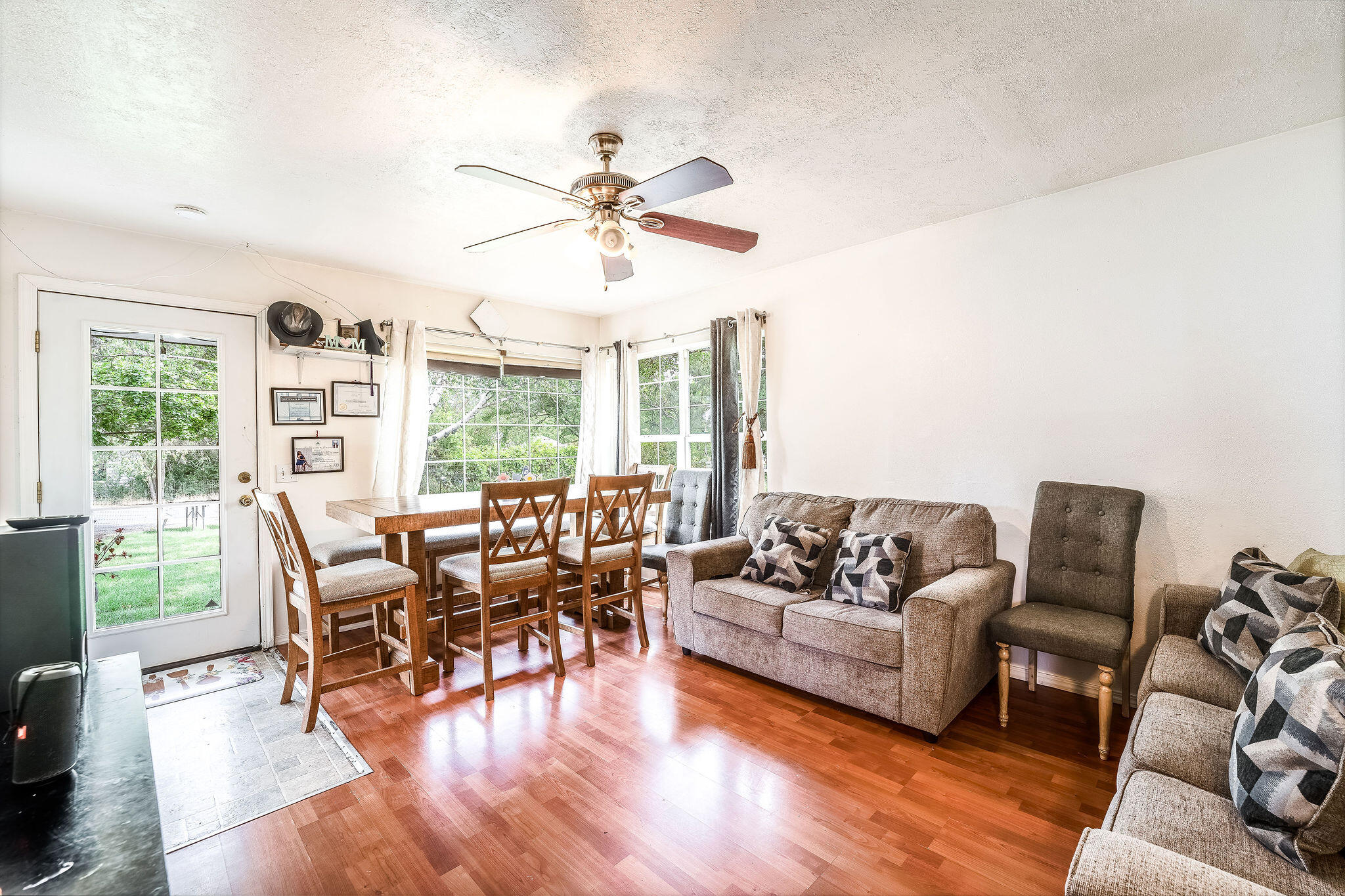 Living and dining room with wood floors, gray seating, a dining table, and large garden-facing windows.