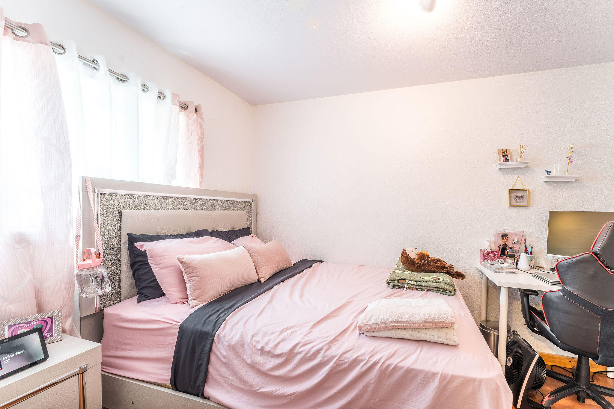 Bedroom with pink bedding, a glittery headboard, and a desk with a gaming chair.