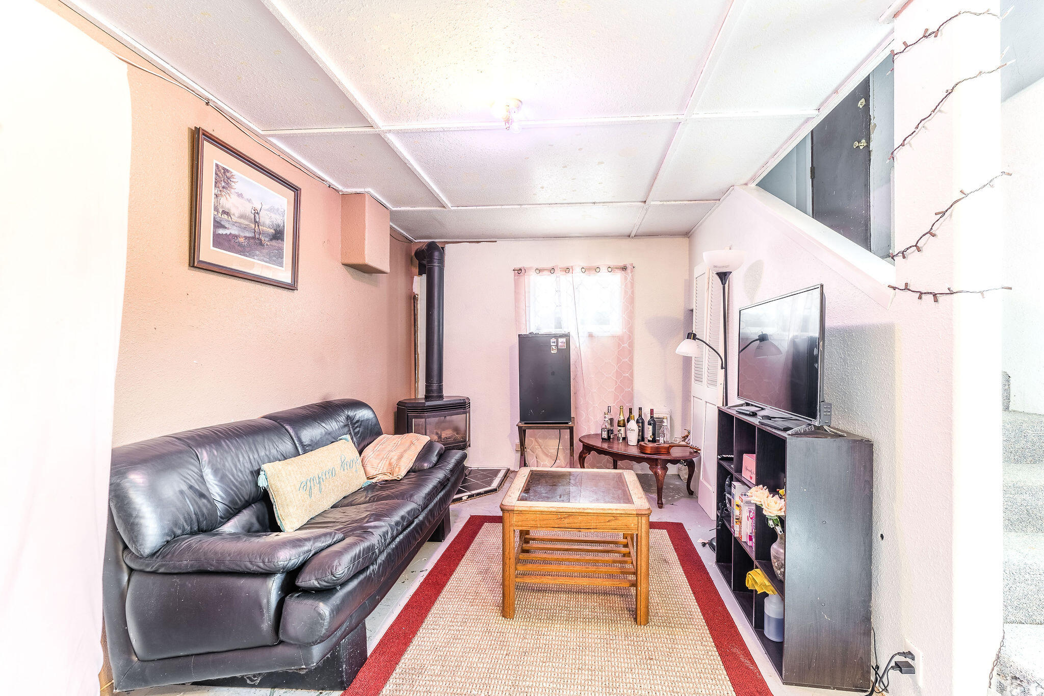 Living room with a leather sofa, wood-burning stove, and red-bordered rug.