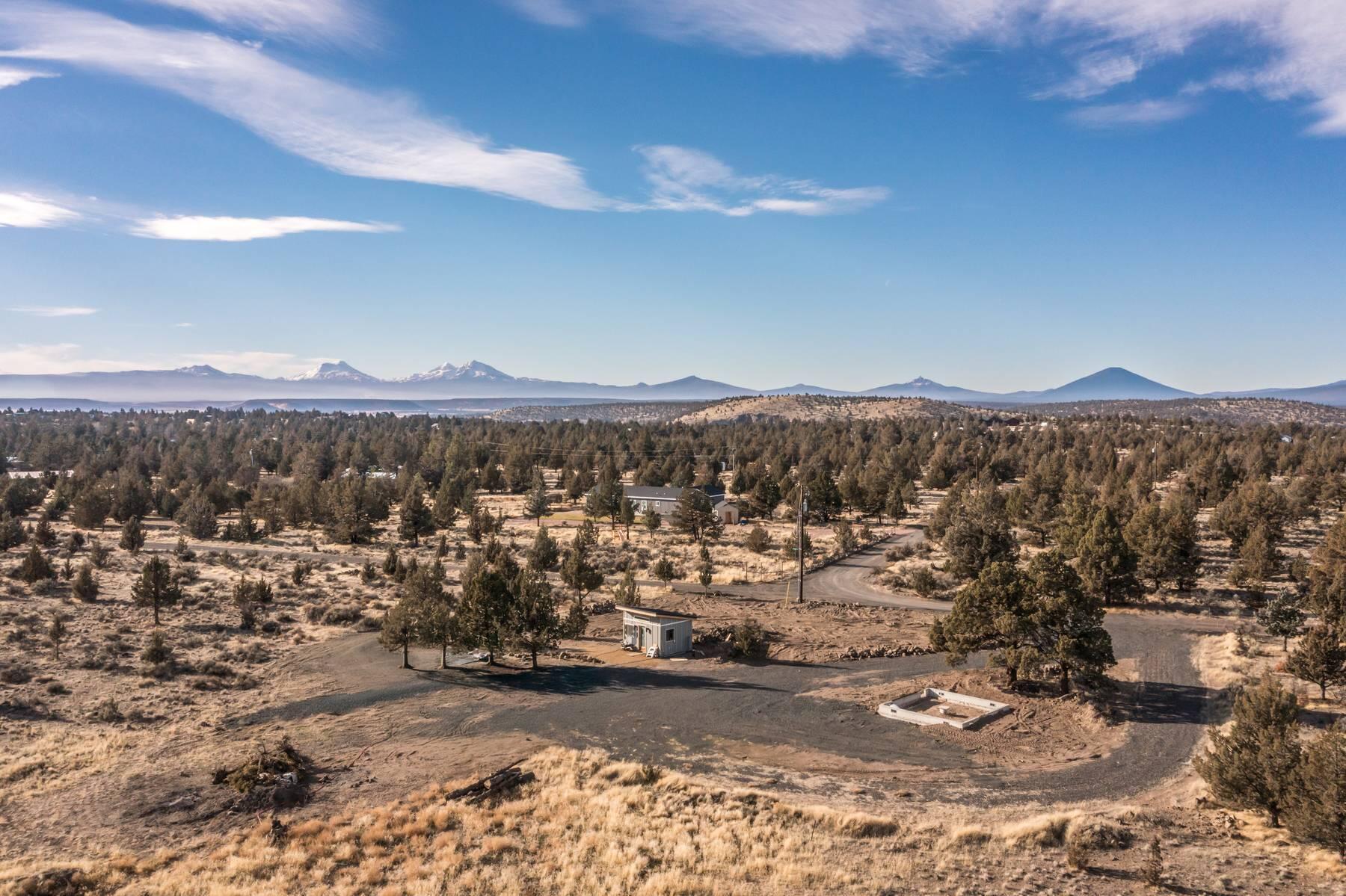 Aerial view of a dry, tree-dotted lot with a small outbuilding and distant snowcapped mountains.