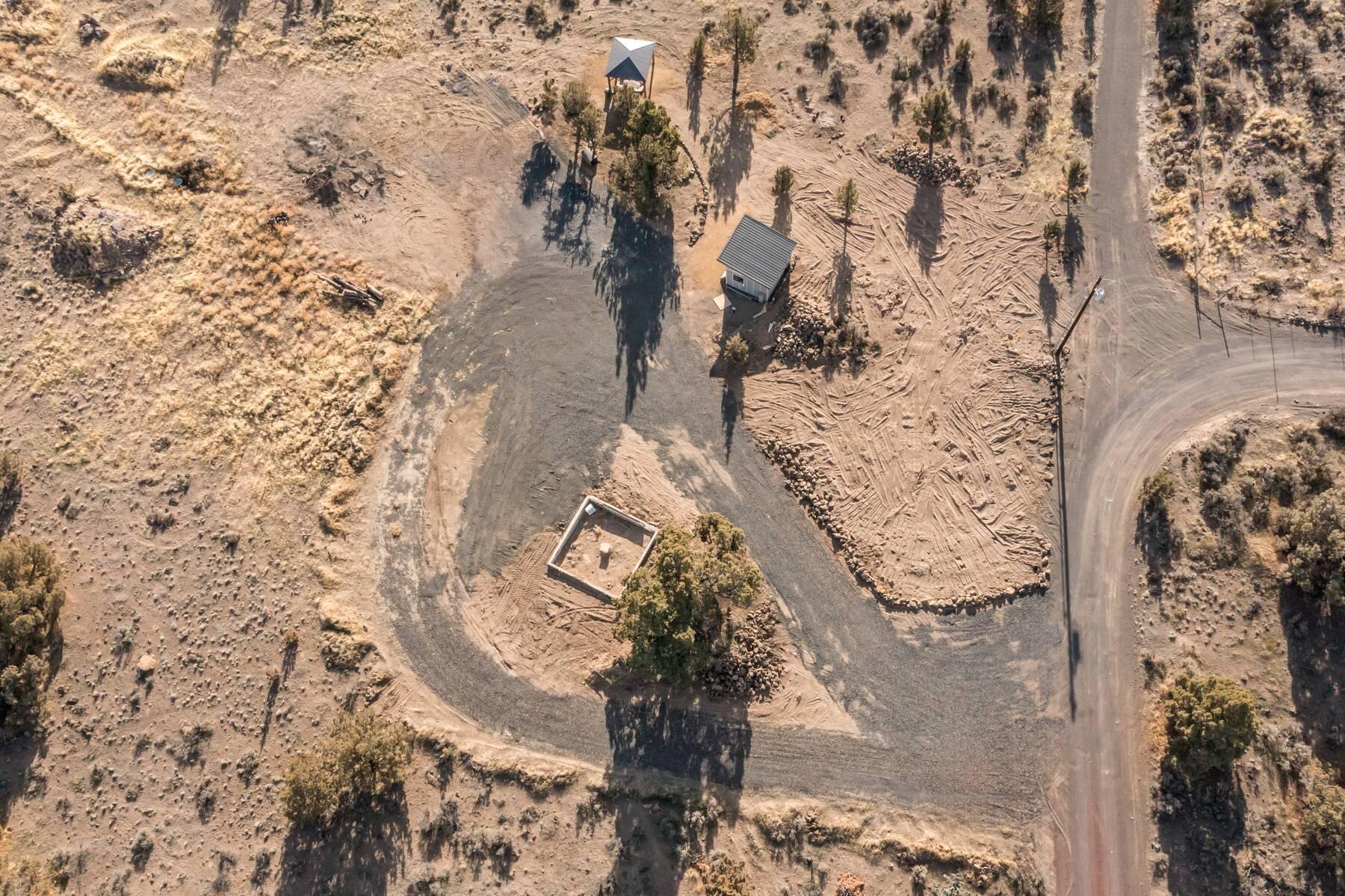 Aerial view of a graded lot with a small foundation, shed, and gravel drive