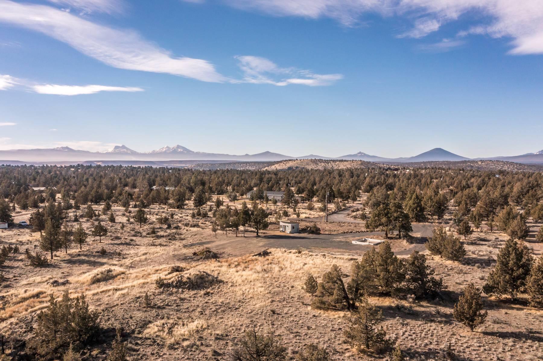 Aerial view of a vacant high-desert lot with scattered trees and distant snow-capped mountains.