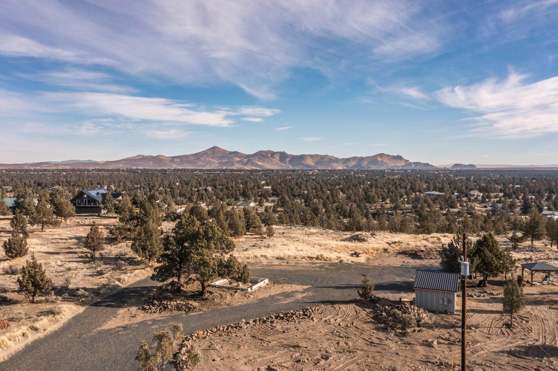 Vacant lot with gravel access, scattered evergreens, and distant mountains.