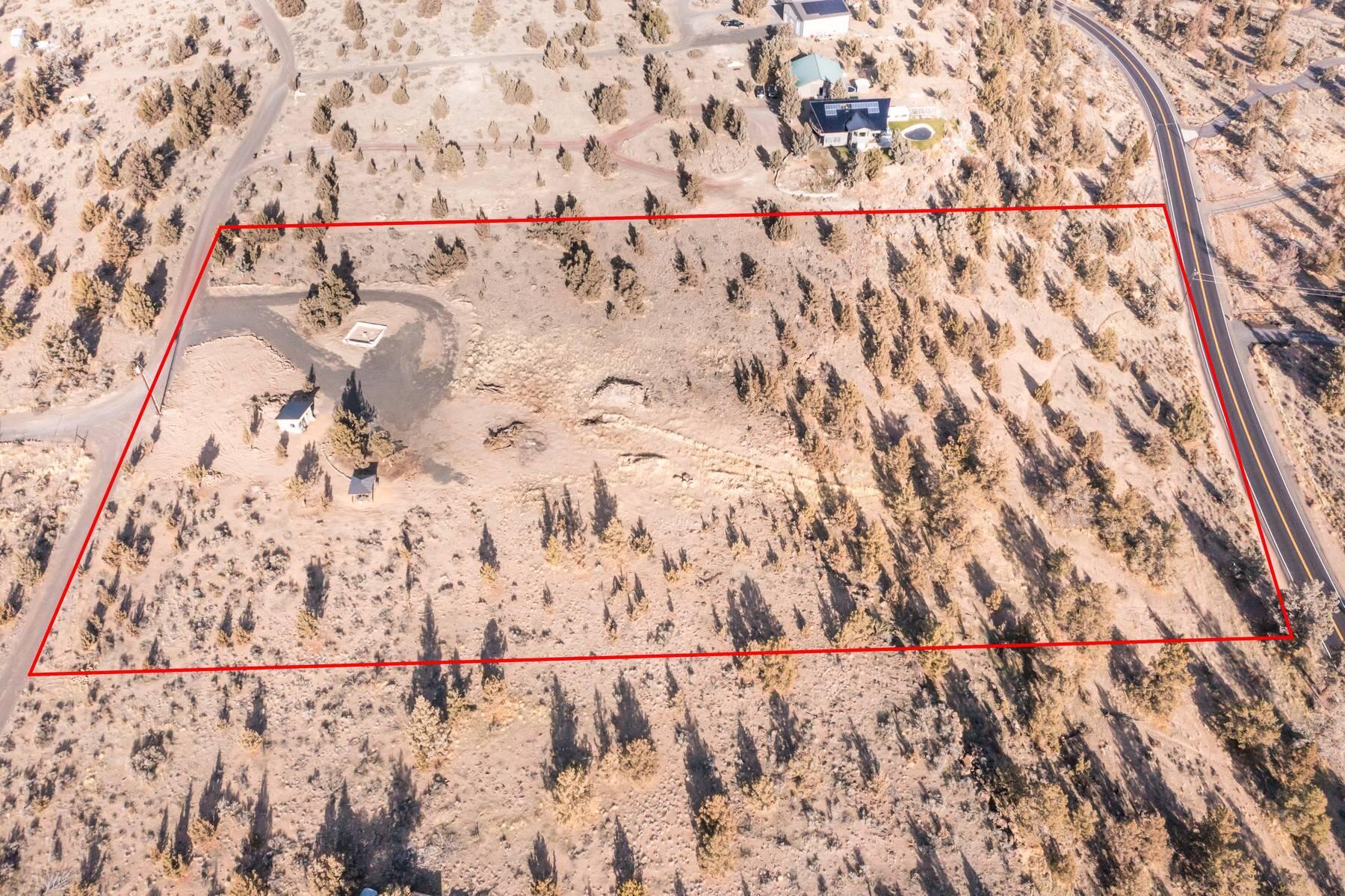 Aerial view of a dry, scrub-covered lot outlined in red beside a paved road.