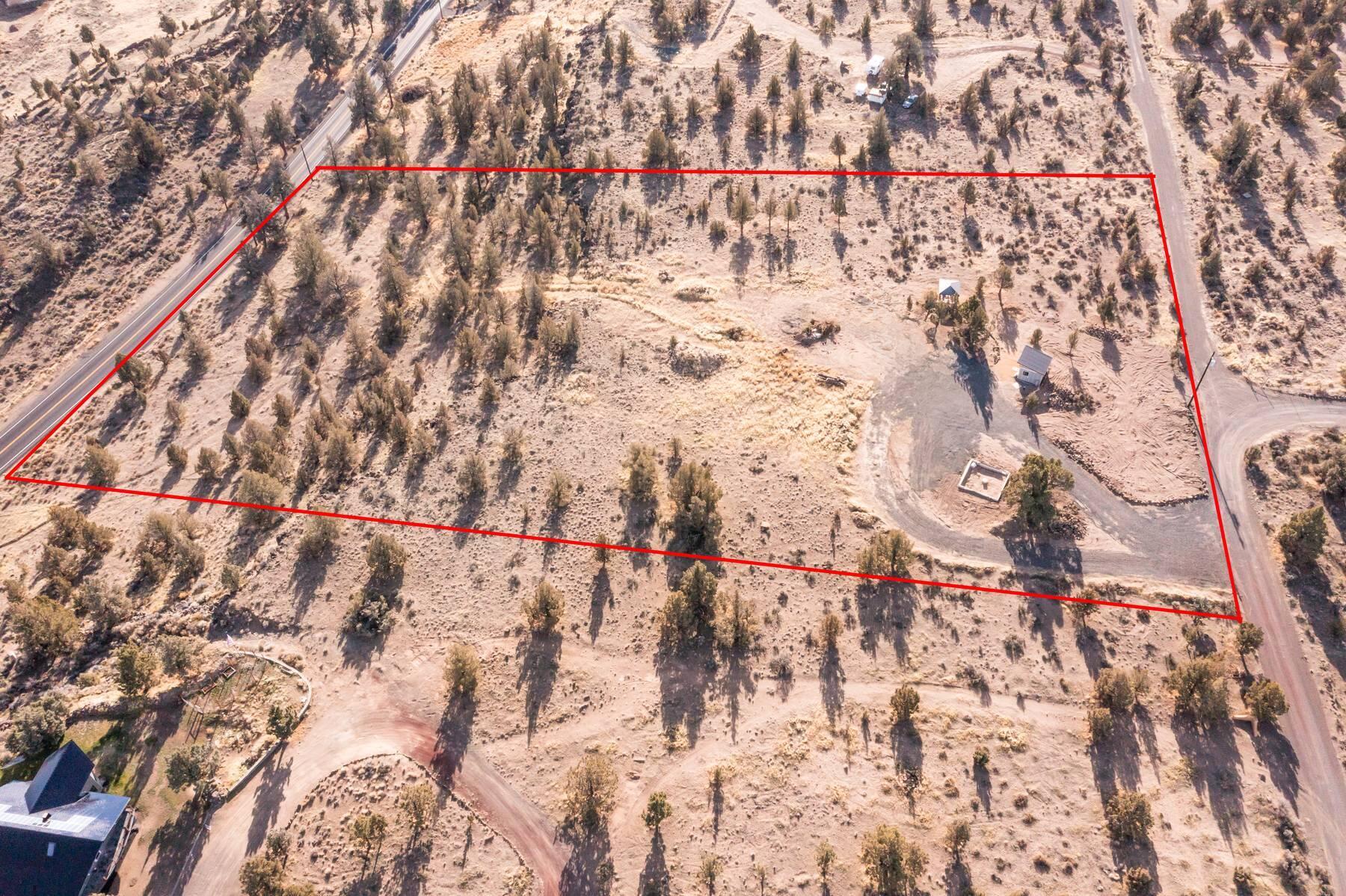 Aerial view of a scrub-covered lot outlined in red, with roads along two sides and a few small structures.