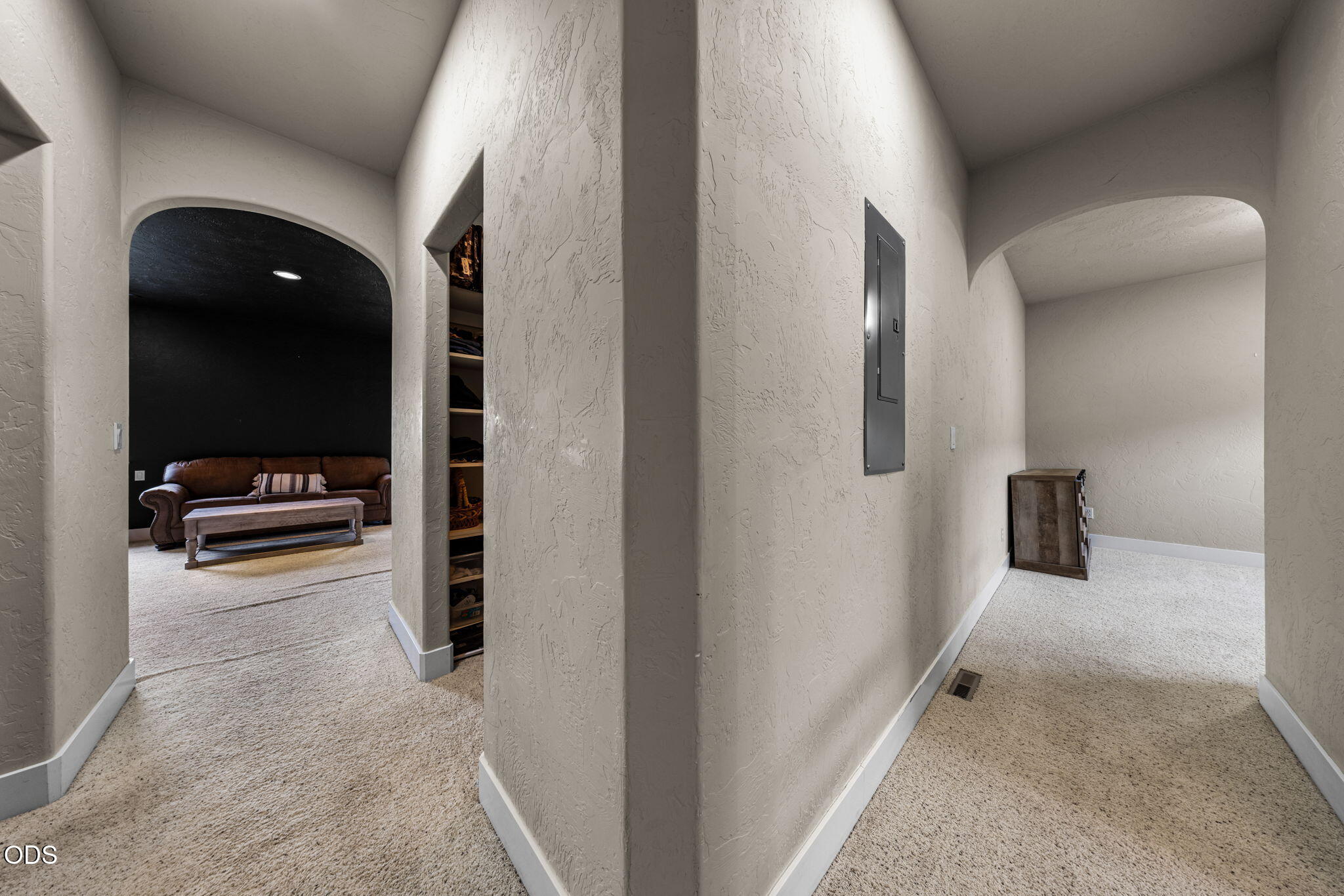 Carpeted hallway with arched openings and a view into a dark-walled sitting room.