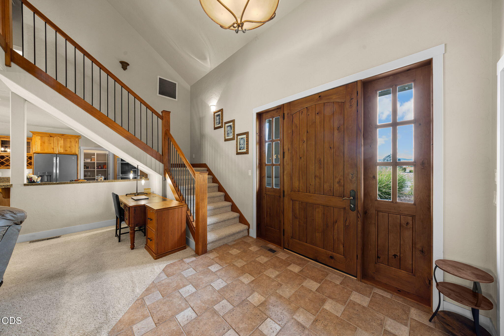 Foyer with a tall wooden front door, tiled floor, and carpeted staircase.