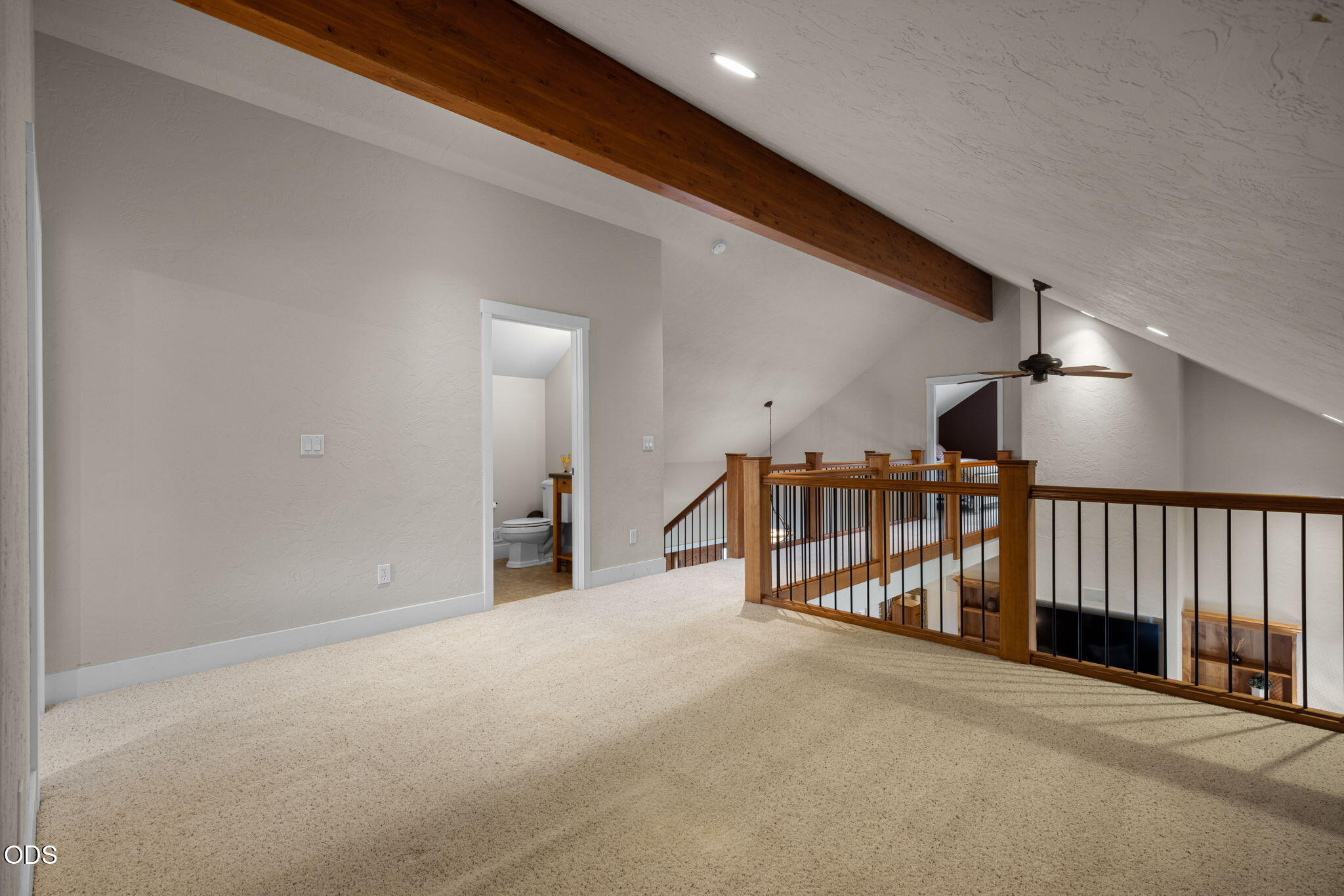Carpeted loft landing with a vaulted ceiling, exposed wood beam, and railing overlooking the lower level.