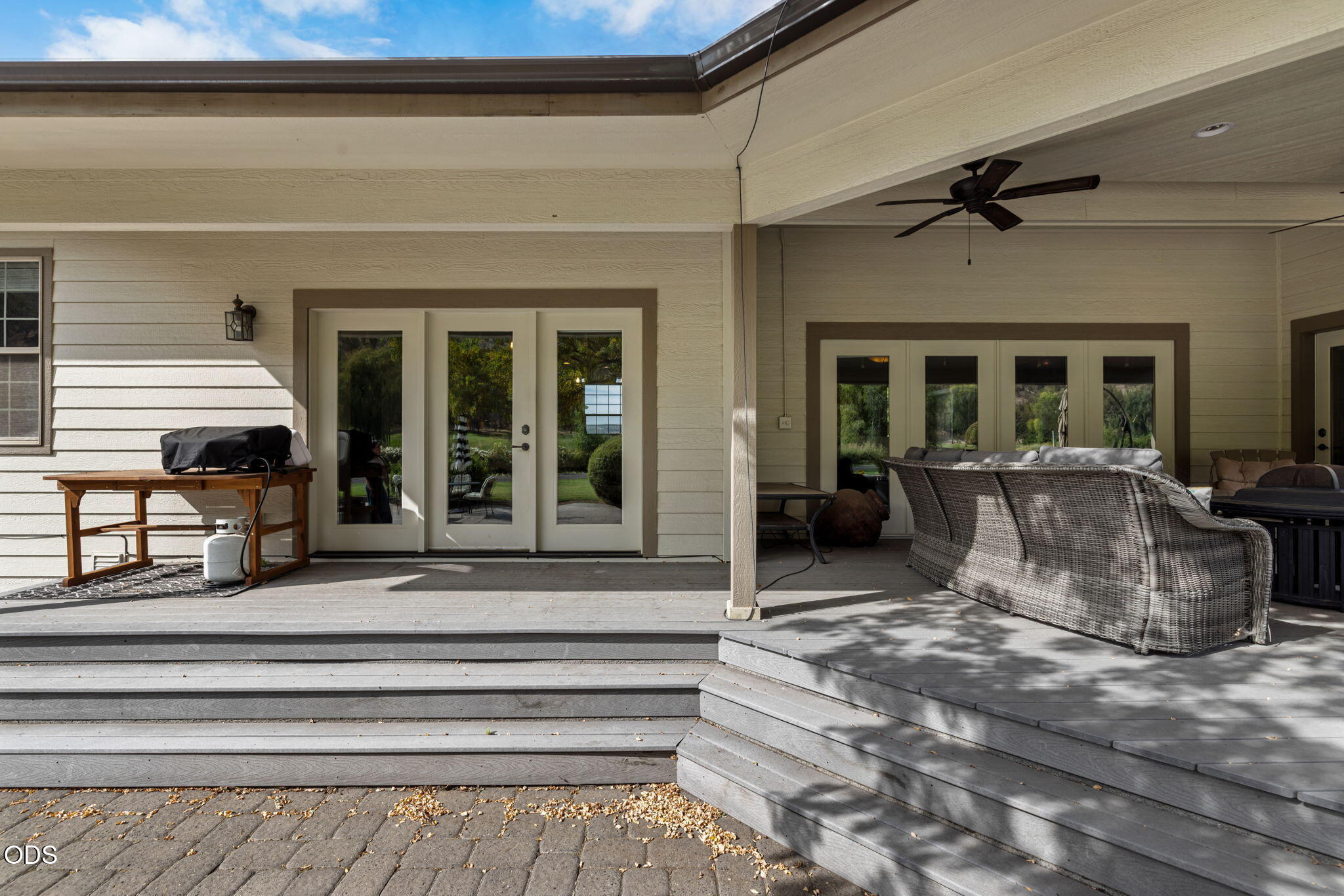 Covered deck with wicker seating, wide gray steps, and glass doors to the home.