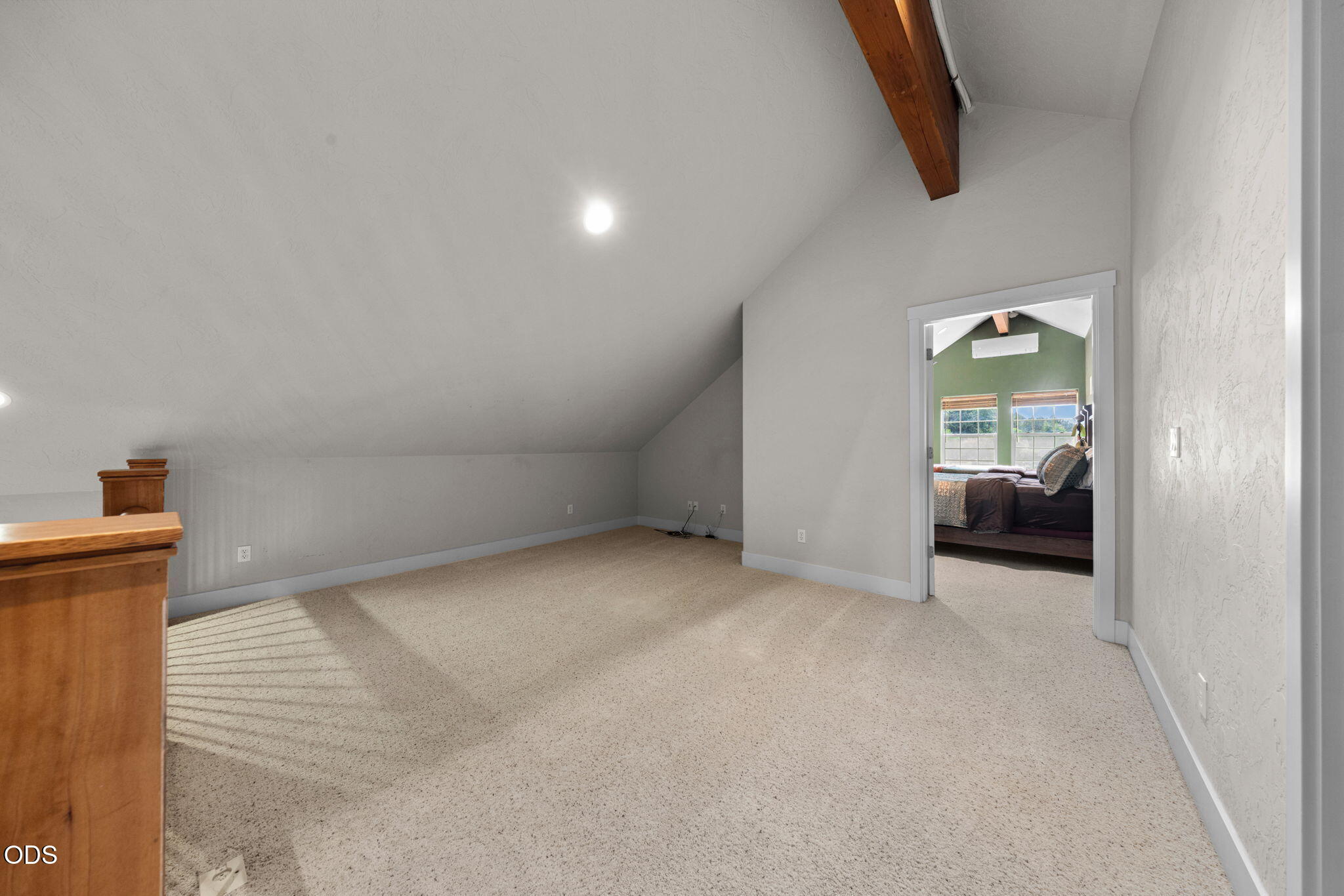 Carpeted bonus room with a sloped ceiling, exposed beam, and doorway to a bedroom.
