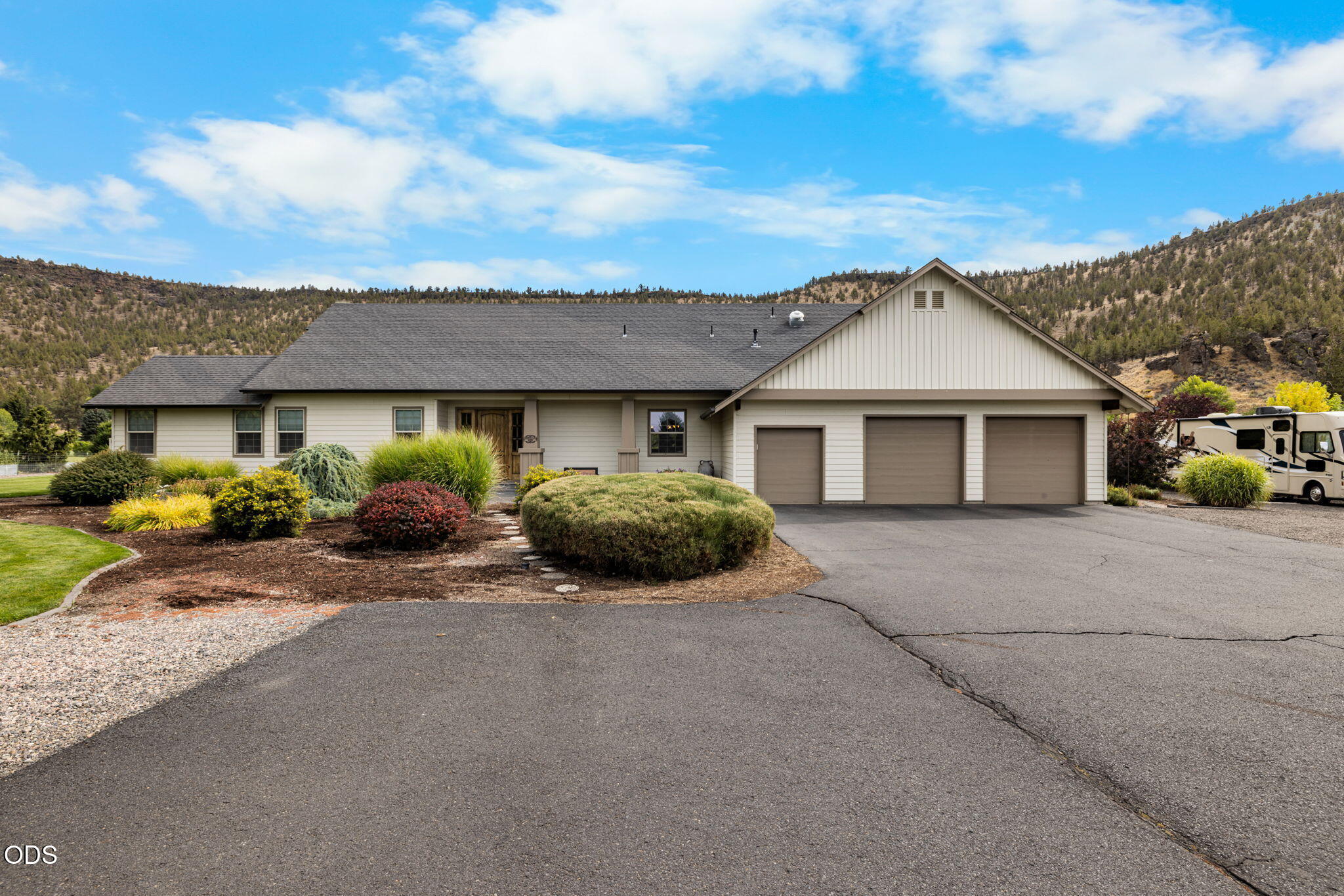 Home with three-car garage, landscaped yard, wide driveway, and wooded hills behind it.