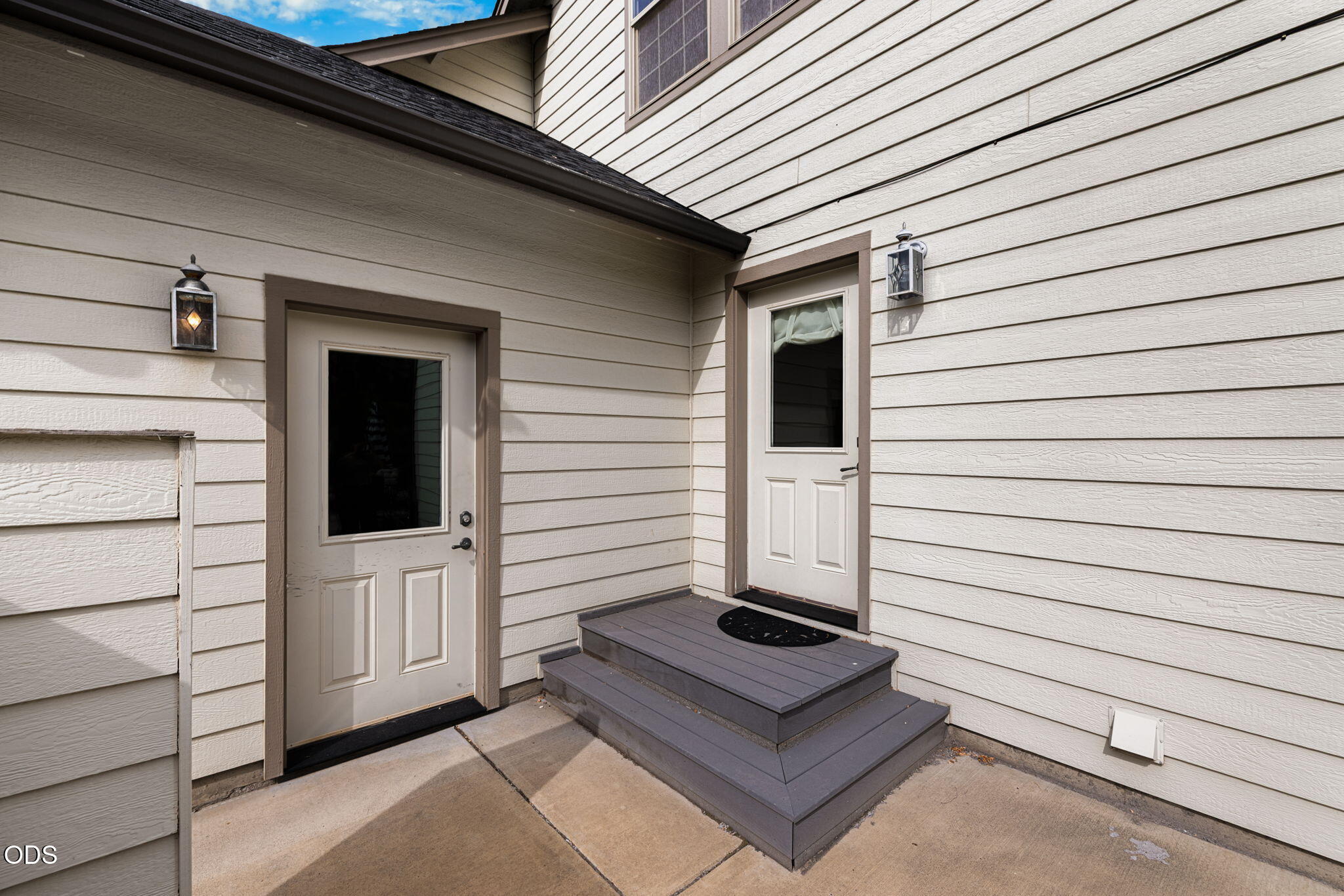 House entry with two white doors, gray steps, and wall lanterns.