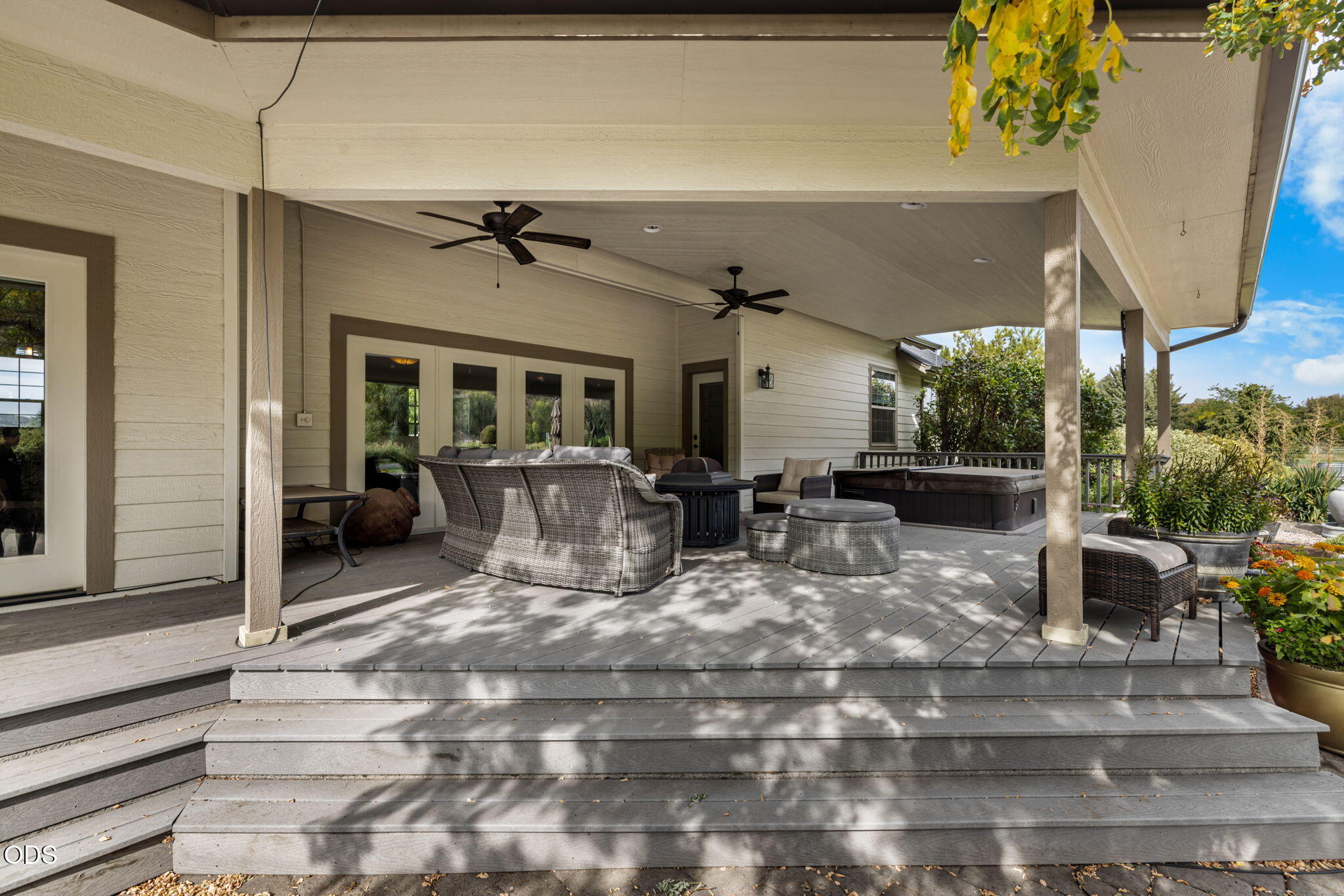 Covered deck with wicker seating, two ceiling fans, and a hot tub beside the garden.